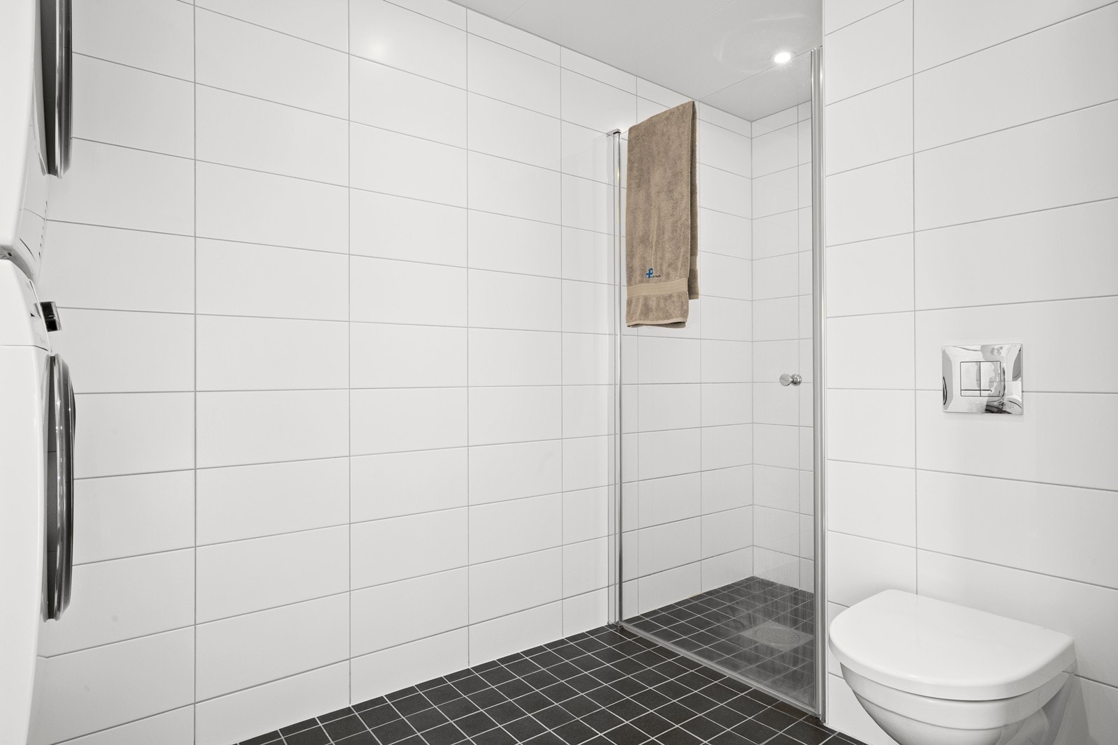 Pent flislagt bad/vaskerom. Rommet har innredning med nedfelt servant, veggfestet toalett, dusjhjørne og opplegg for vaskemaskin. Galleribilde