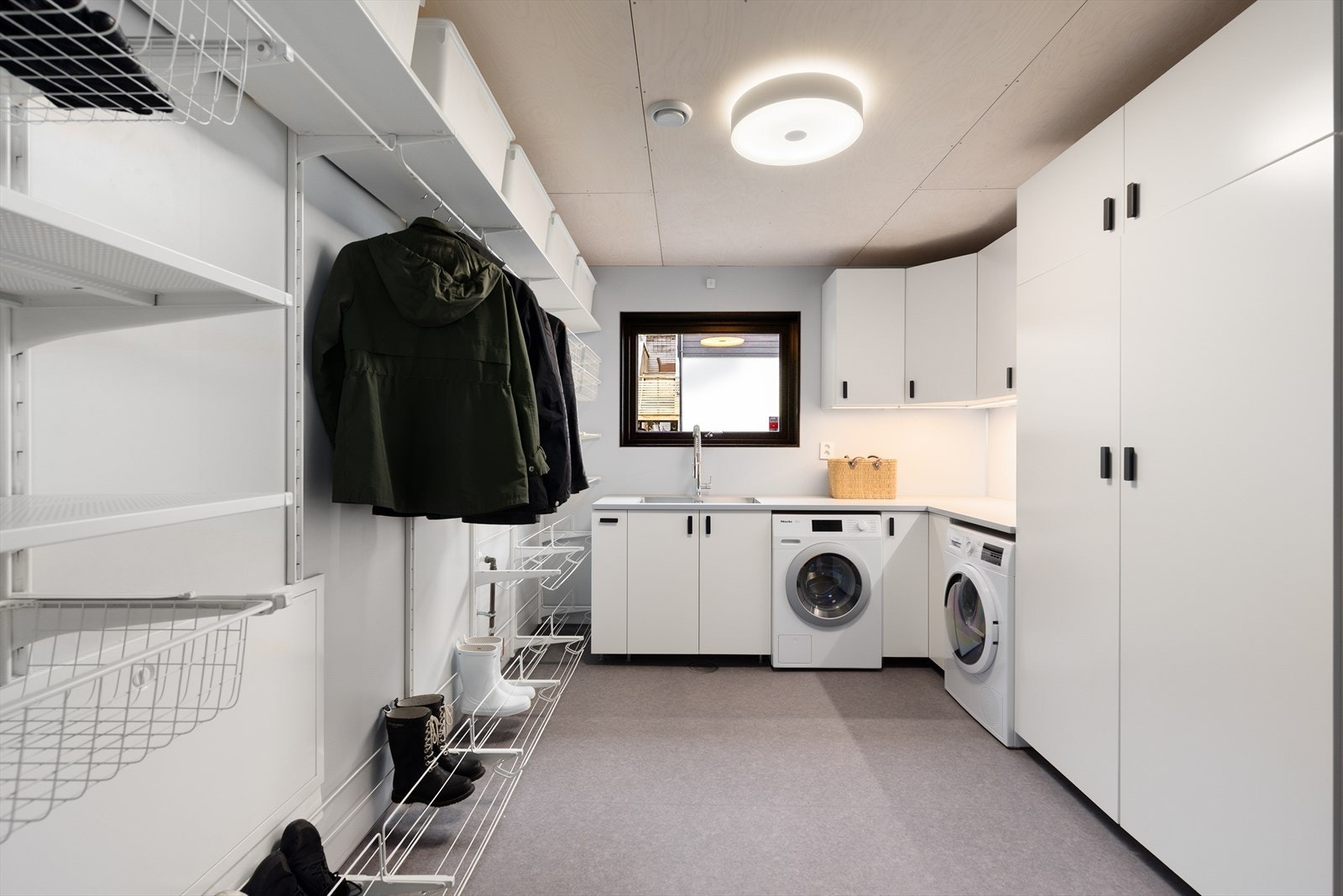 Eget vaskerom i 1. etasje, med praktisk innredning og åpen garderobe på vegg. Det er avsatt plass til vaskemaskin og tørketrommel under benk. Galleribilde
