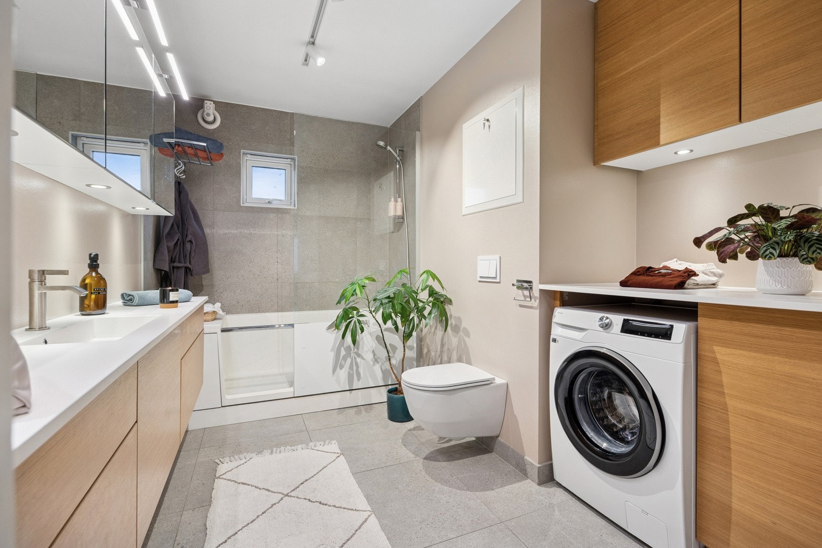 Badet har en kombinert dusj og badekar med praktisk glassdør, samt flott løsning for vaskemaskin med god oppbevaringsplass og arbeidsbenk. Galleribilde