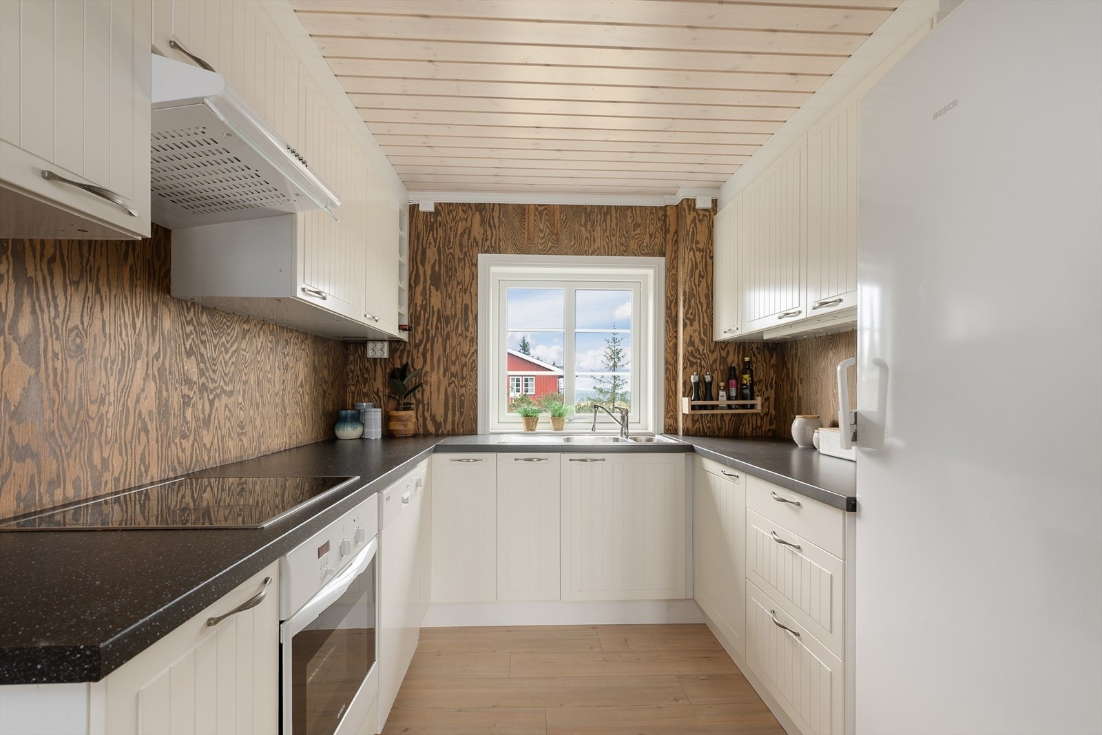 Pent og praktisk kjøkken med innredning plassert i en U-form. Lyse fronter på innredningen med lett profilering. Fint lys inn over kjøkenbenken. Galleribilde