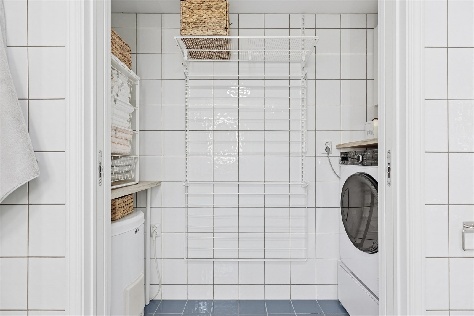 Praktisk vaskerom med direkte adkomst fra badet. God plass til vaskemaskin, tørkemuligheter og oppbevaring, med flislagte vegger for et rent og funksjonelt uttrykk. Galleribilde