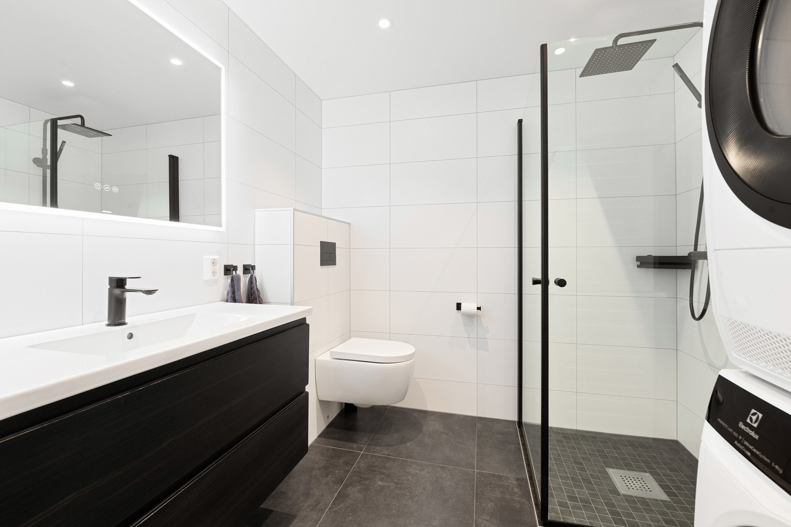 Badet har lekre fliser på gulv og vegger og er innredet med servantskap, dusjhjørne og vegghengt wc. Det er plass til vaskemaskin og tørketrommel. Galleribilde