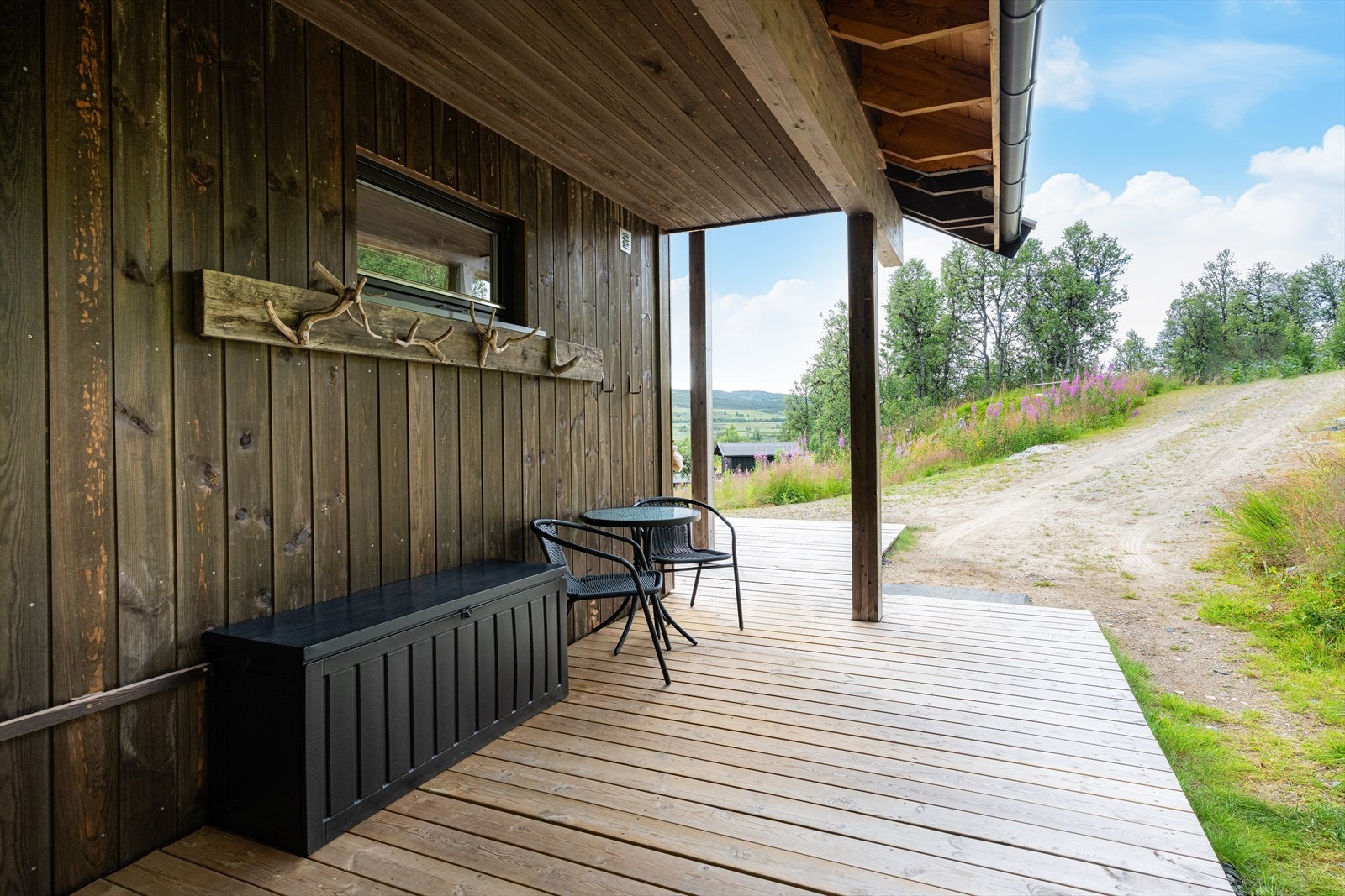 Overbygget inngangsparti til hytta, med god plass for sittegruppe og blomsterpotter. Galleribilde