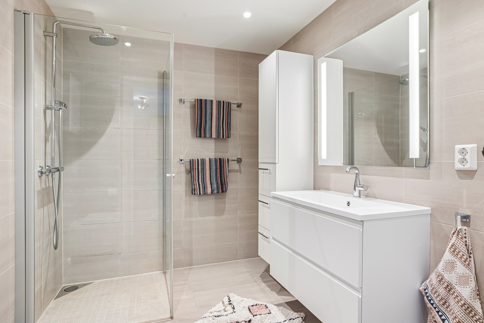 Innredningen består av speil med lys, servant med seksjon, høyskap, veggmontert toalett og dusjhjørne i herdet glass. Galleribilde