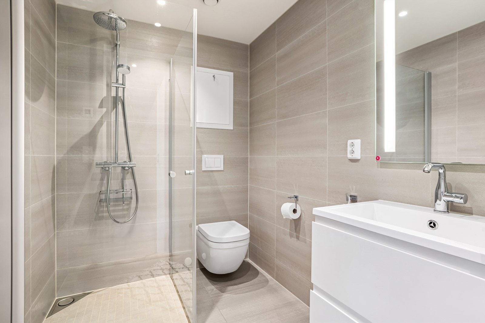 Badet på hovedplan er flislagt, innredet med speil med lys, servant med seksjon, veggmontert toalett og dusjhjørne i herdet glass. Galleribilde