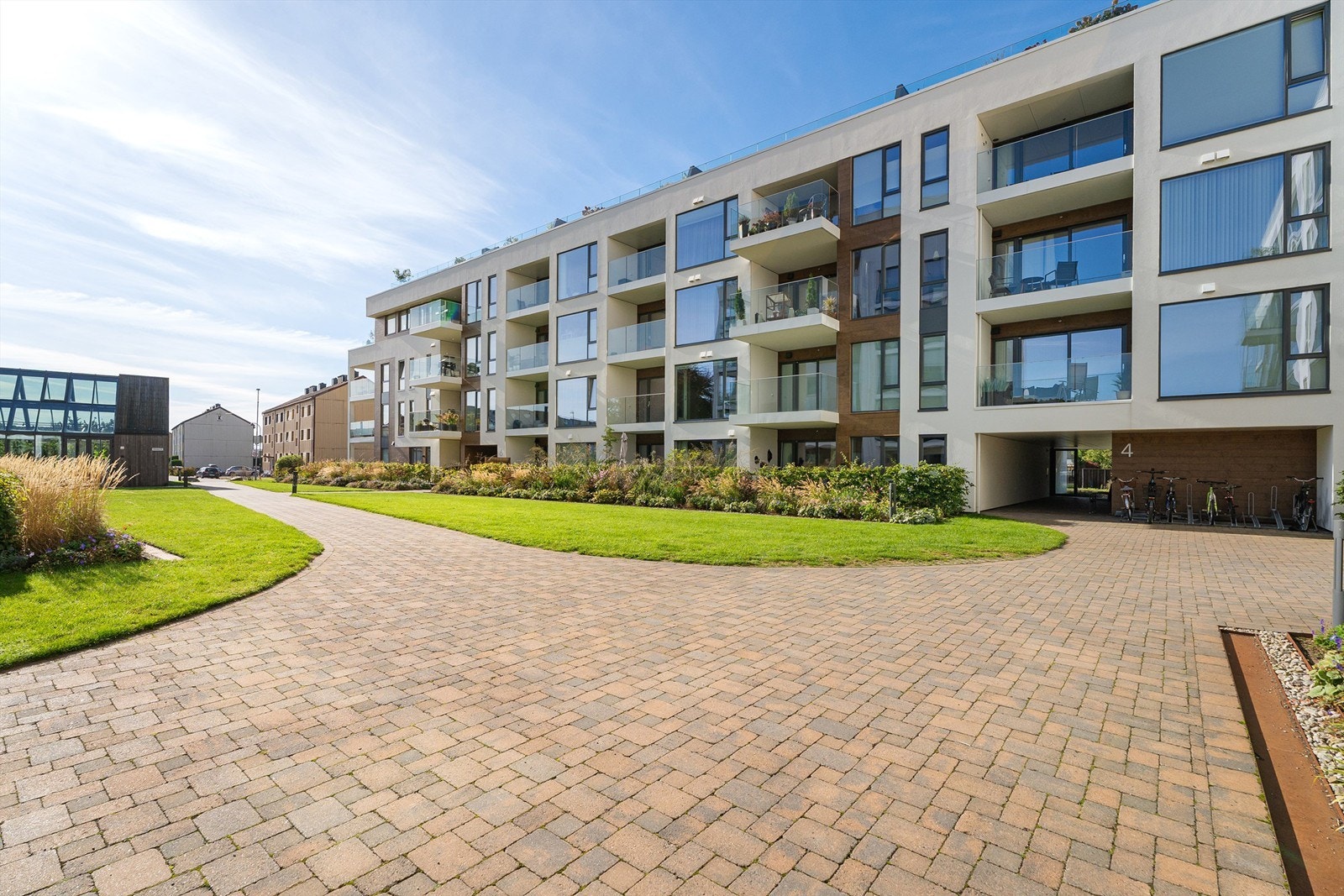 Det er lagt opp til hyggelig beplantning, gressplen og belegningsstein. Videre er det sykkelparkering til høyre. Galleribilde
