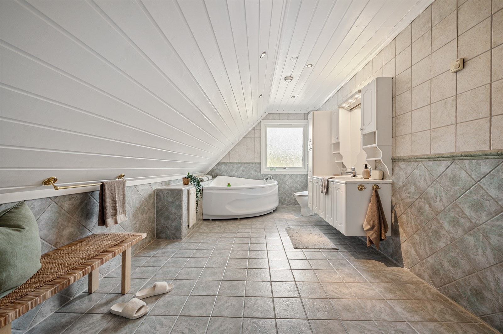 Badet er helfliset og innredet med hjørnebadekar, dusjnisje med innfellbare dører i herdet glass, toalett, veggskap og servant i møblement med nedfelt porselensvask og speil m/belysning. Galleribilde