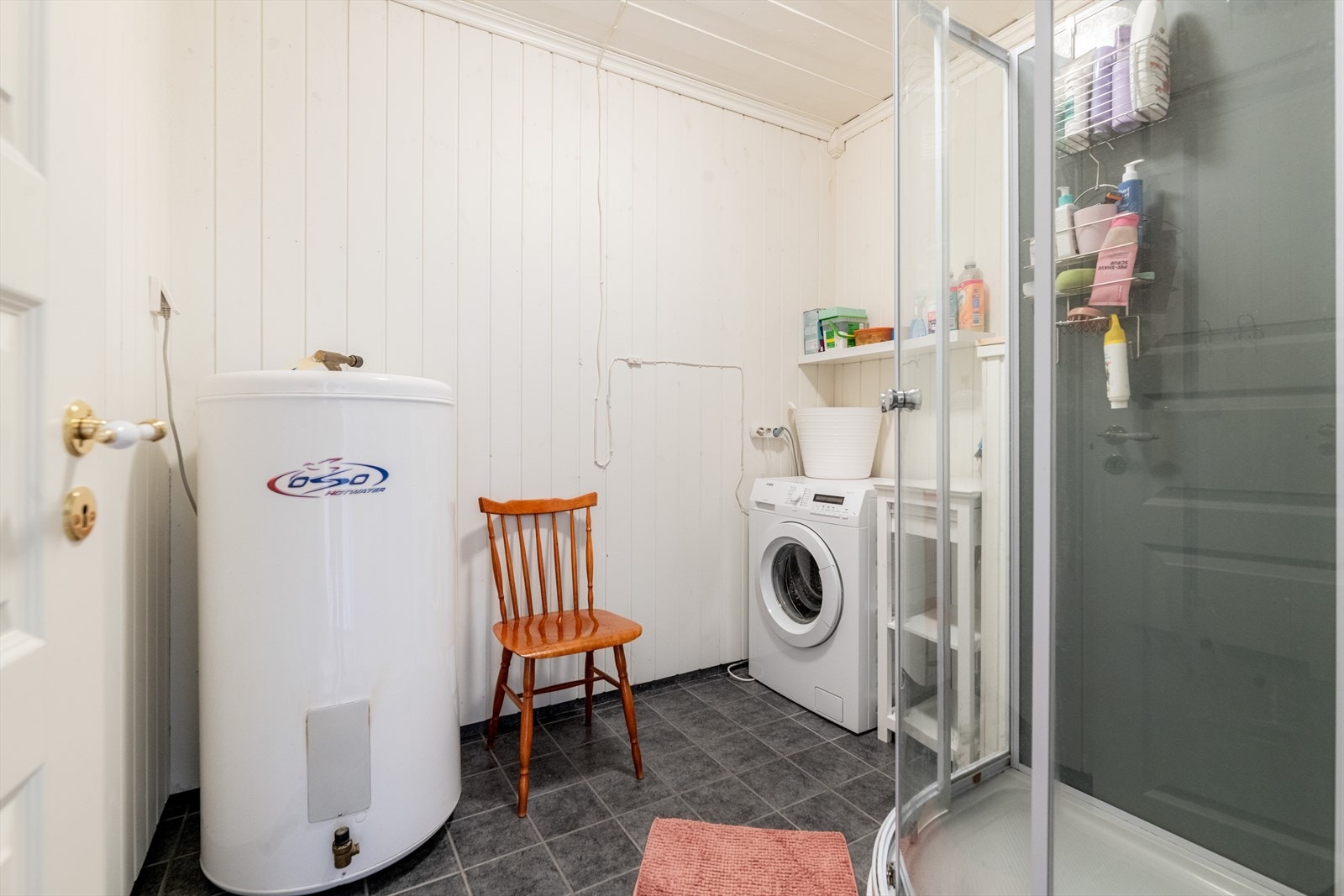 Badet er innredet med dusjkabinett, servantinnredning og opplegg for vaskemaskin. Det er flis på gulv med gulvvarme og panel på vegger. Galleribilde