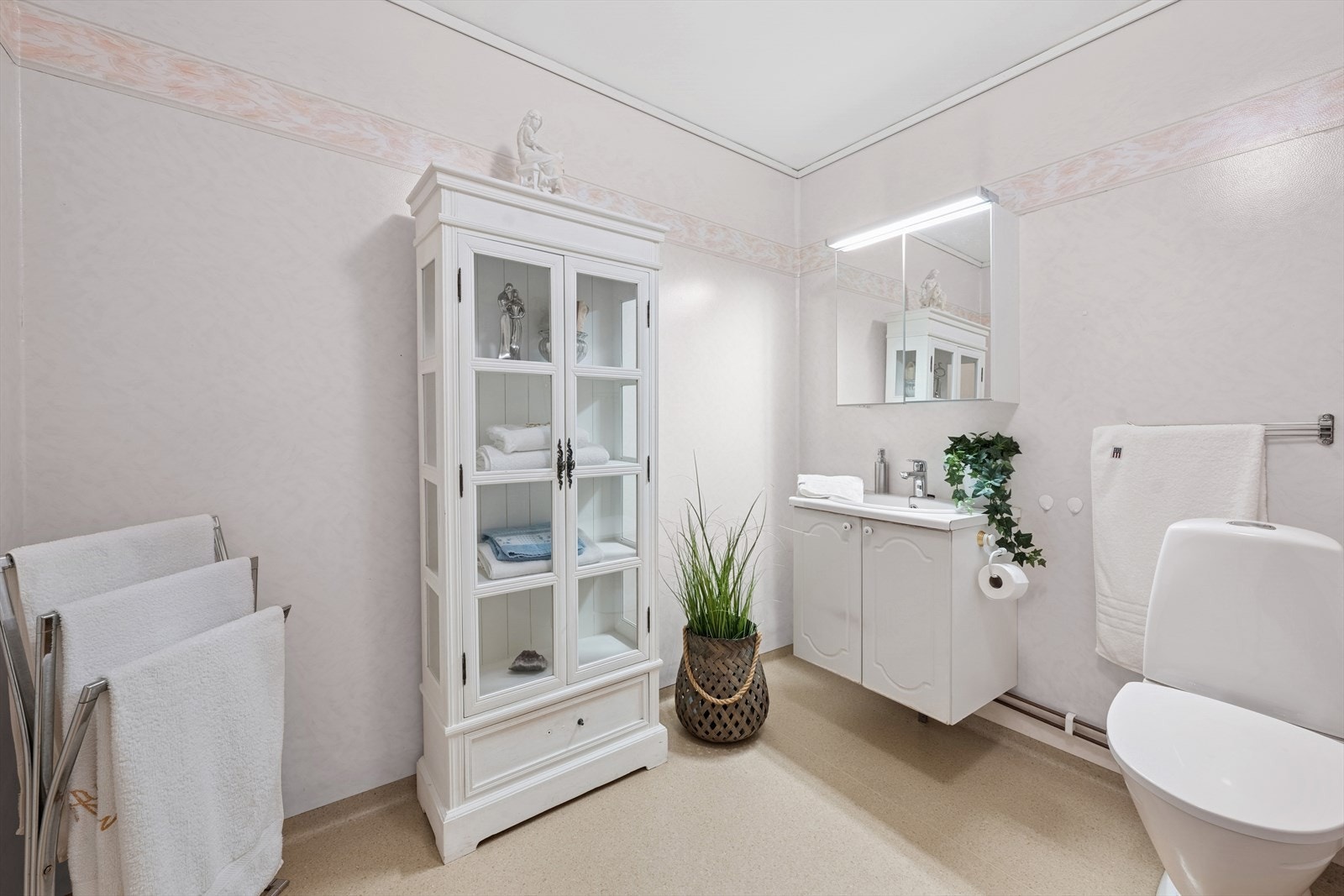 Romslig baderom innredet med servant med skap, gulvmontert toalett og opplegg til vaskemaskin og tørketrommel. Galleribilde