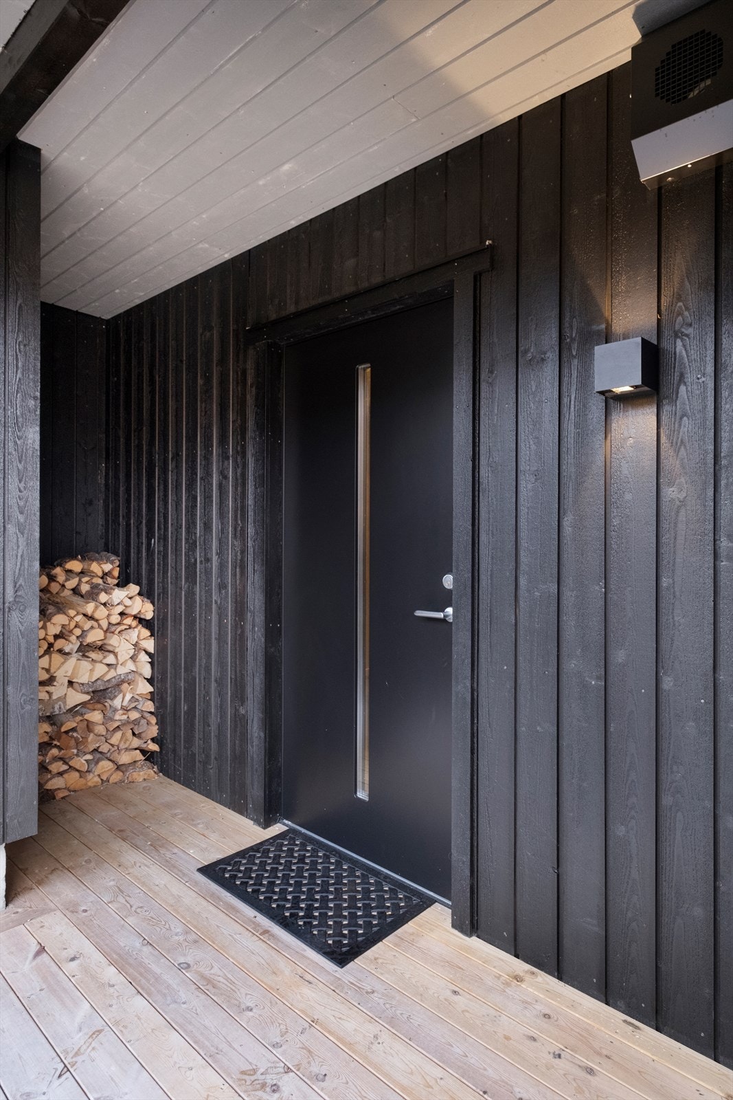 Overbygd inngangsparti beskytter mot vær og vind, med stående bordkledning i treverk. Galleribilde