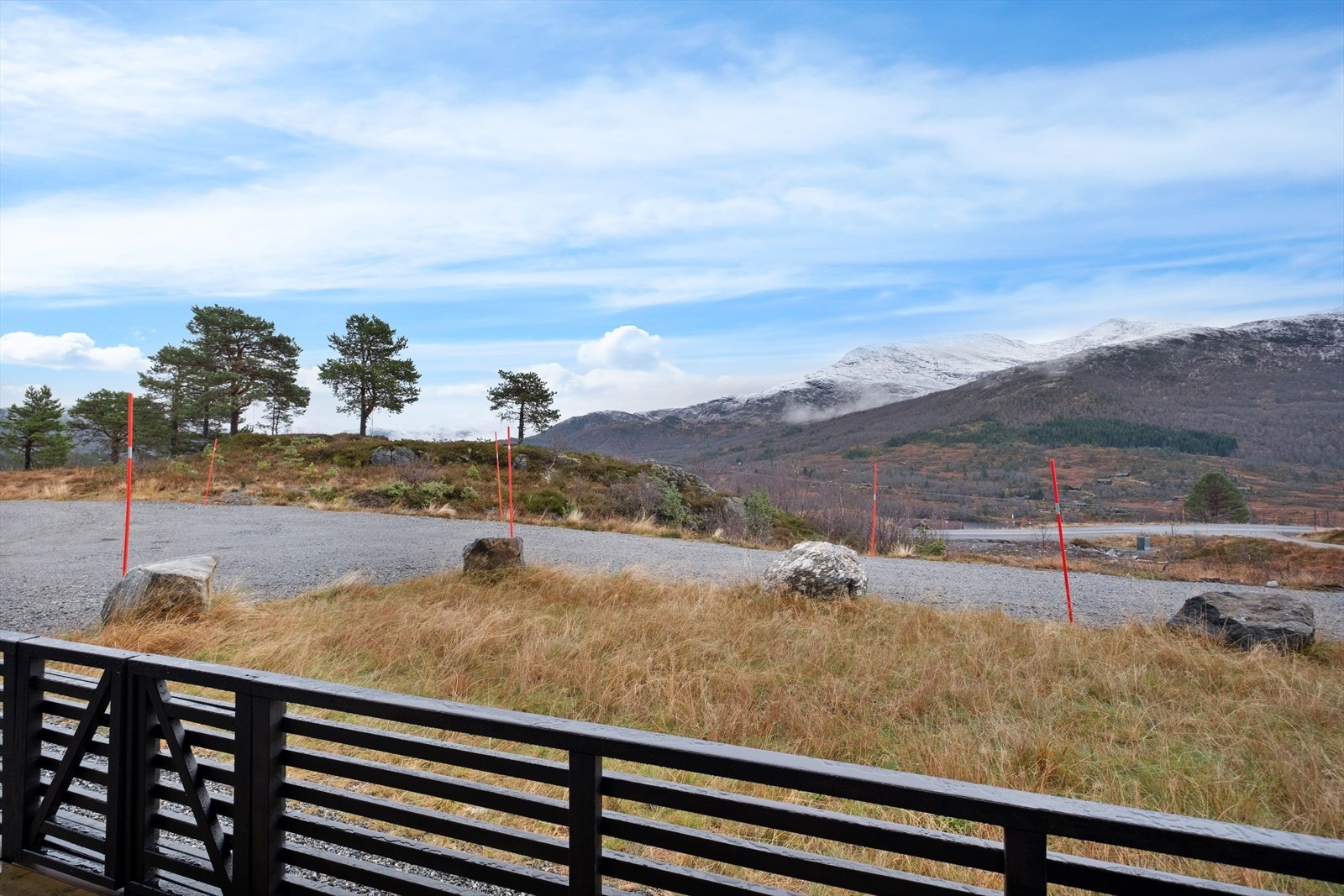 Utsikt fra eiendommen viser det flotte fjellandskapet og gruslagt innkjørsel med biloppstillingsplass. Galleribilde