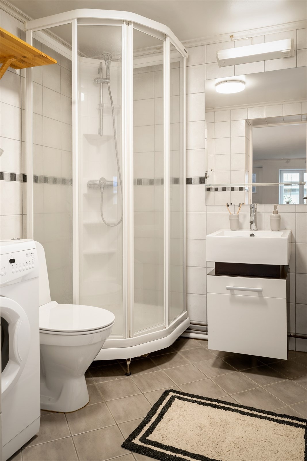 Badet inneholder heldekkende servantskap med glatte fronter, gulvstående klosett, dusjkabinett med termostatstyrt blandebatteri og opplegg for vaskemaskin. Galleribilde