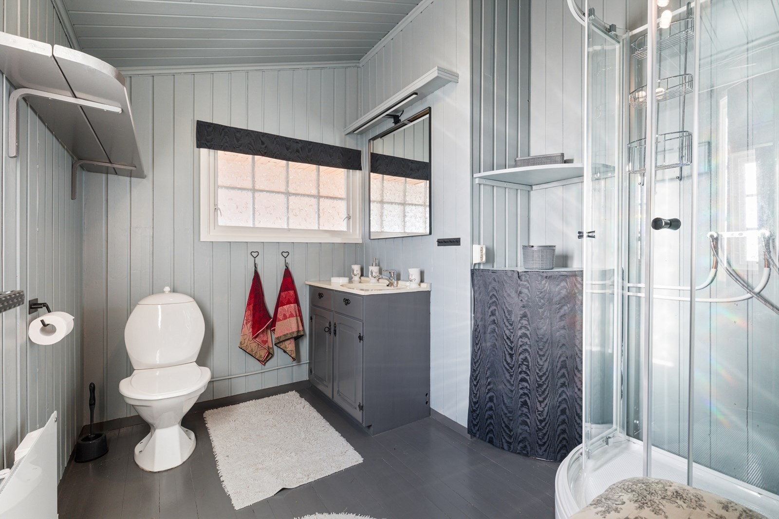Badet har malte gulvbord og malt panel på vegger og i tak | rommet er utstyrt med baderomsinnredning, dusjkabinett og wc Galleribilde
