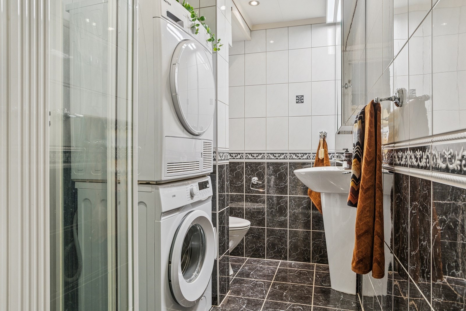 Badet er helfliset og inneholder toalett, vask og dusjhjørne med vegger. Vaskemaskin og tørketrommel følger salget Galleribilde
