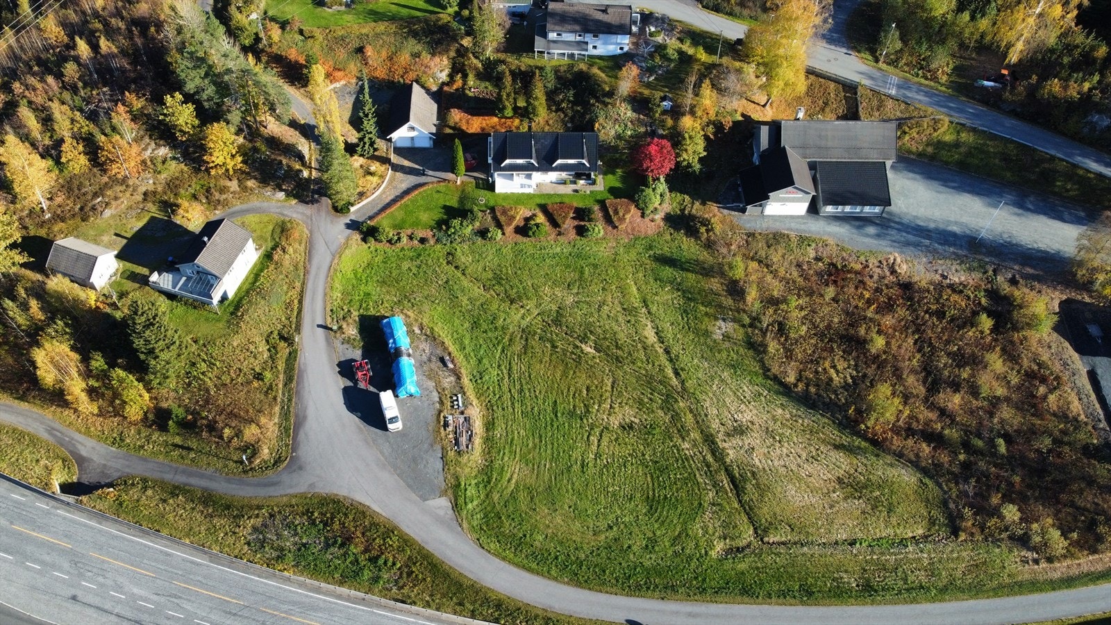 Eiendommen sett ovenfra - pent opparbeidet tomt med gårdsplass, garasje og solrike uteområder omgitt av frodig natur Galleribilde
