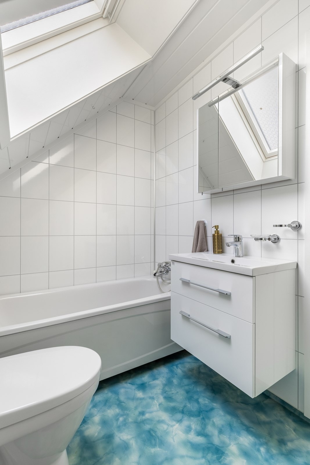 Lyst og moderne bad med badekar, hvite fliser og takvindu som slipper inn rikelig med dagslys Galleribilde