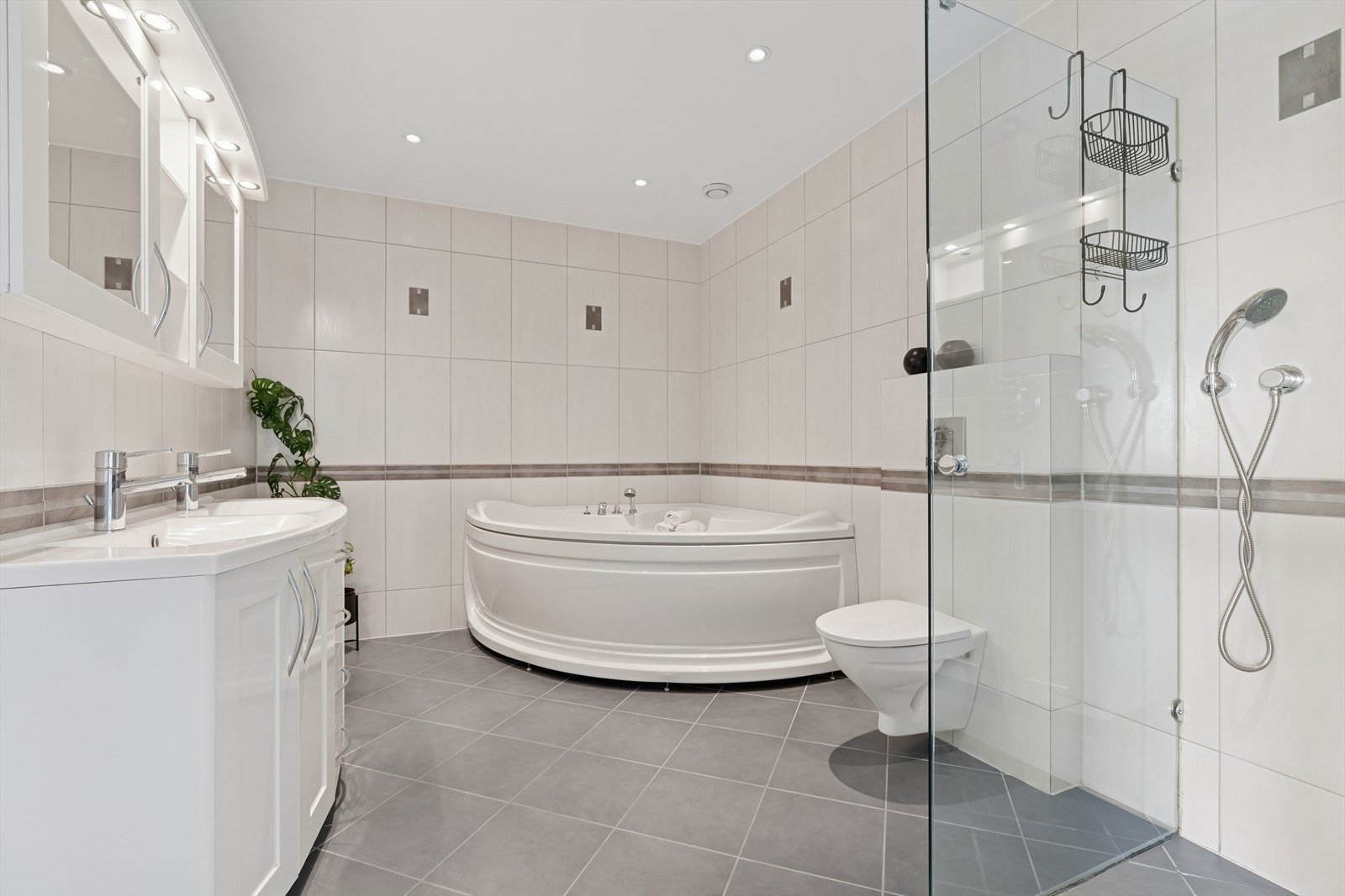 Stort og tidløst innredet baderom i første etasje i tilsvarende stil som de andre baderommene i boligen. Badet er i dag utstyrt med dusjhjørne, hjørnebadekar, veggehngt toalett og veggseksjon med dobbel servant. Galleribilde