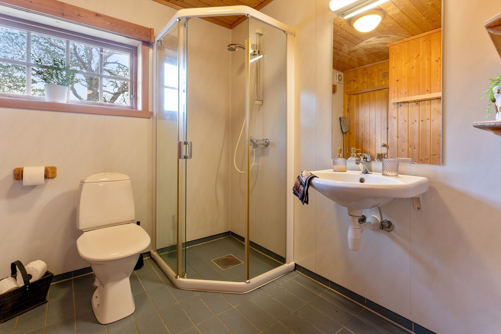 Bad frå byggeår med flis på golv og baderomsplater på vegg. Det er dusj på golv, veggmontert servant og golvståande toalett Galleribilde