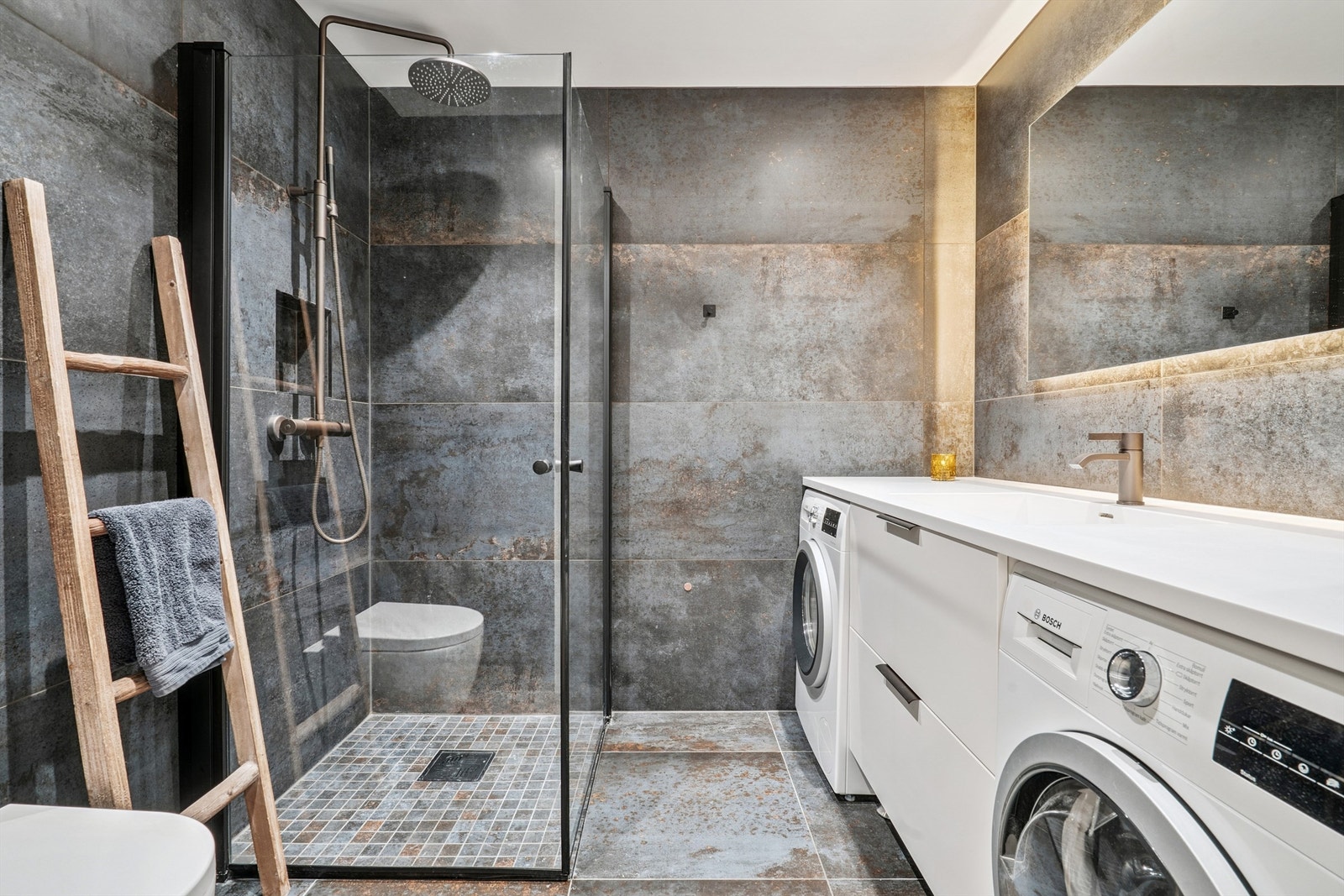 Delikat, flislagt bad med direkte adkomst fra soverommet. Badet inneholder dusjhjørne og praktisk vaskeromsdel med opplegg for vaskemaskin og tørketrommel. Galleribilde