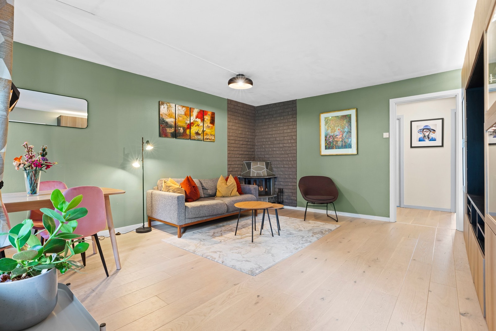 Leiligheten har en lys og innbydende stue med enstavs eikeparkett på gulvet, vegger malt i moderne tone og vedovn i hjørnet. Galleribilde
