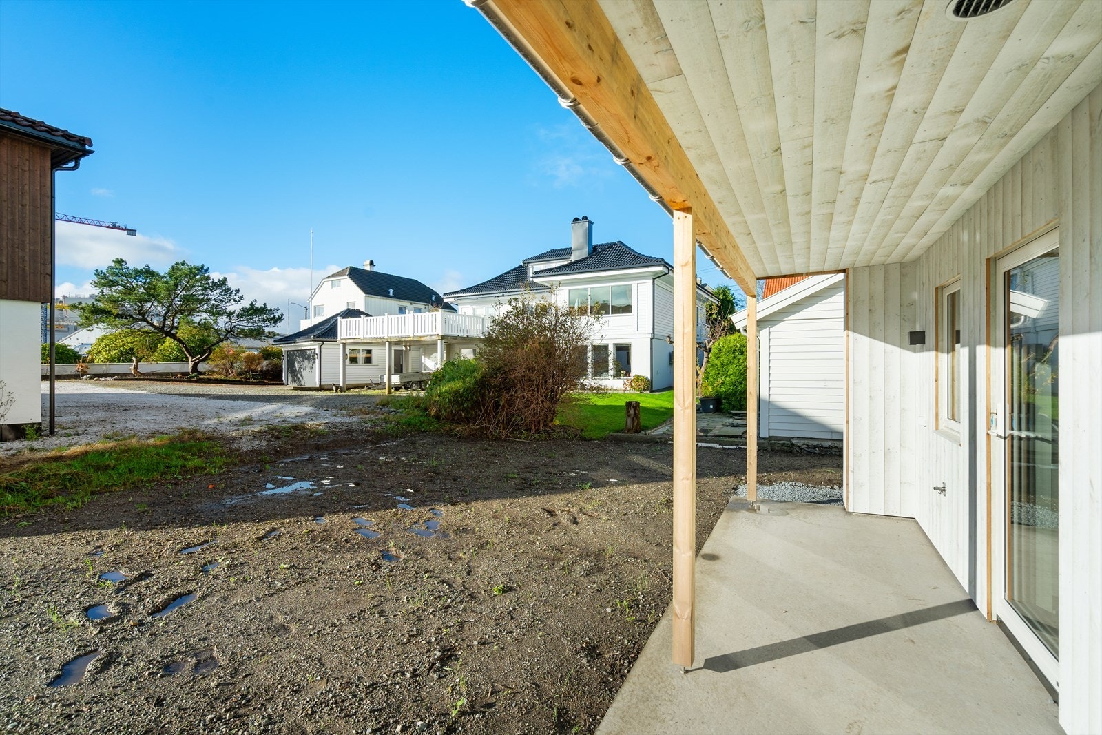 Vestvendt og overbygget betongplatting med utgang til hage med boltreplass til utelek og trampoline Galleribilde