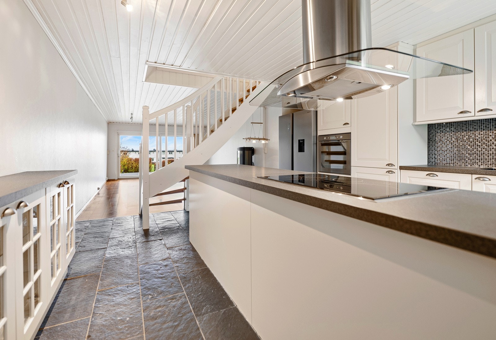 Overgangen mellom stuen og kjøkkenet er markert med parkettgulv i stuen og lekre skiferfliser på kjøkkengulvet. Galleribilde