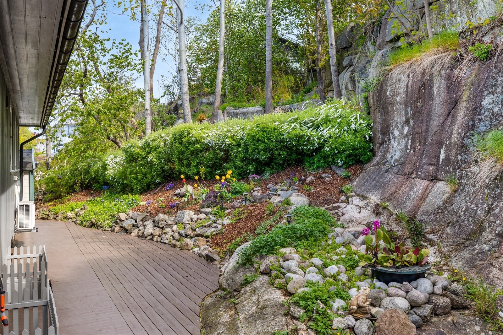 På baksioden av huset er det satt opp platting og utnyttet den plassen man har til det fulle. Plattingen glir inn i naturtomten med fjell og flotte opparbeidede blomsterbed. Galleribilde