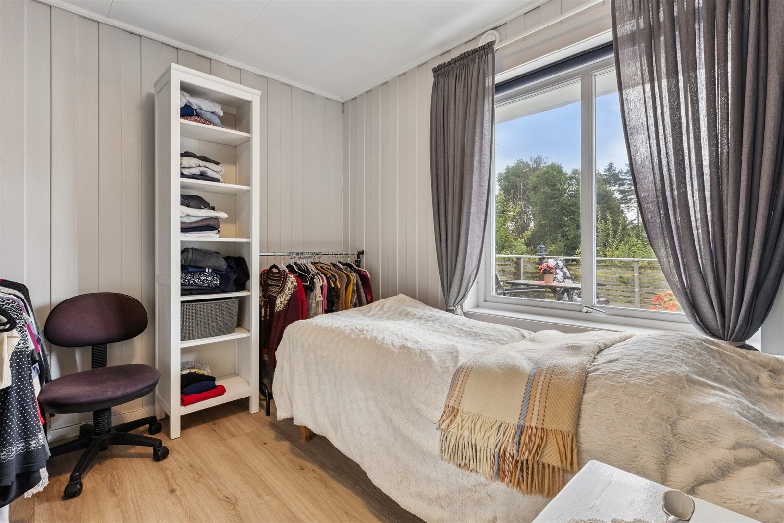 Det er et soverom i dette huset med utsikt ut mot terrassen og hagen. Lysmalte panelvegger. Galleribilde