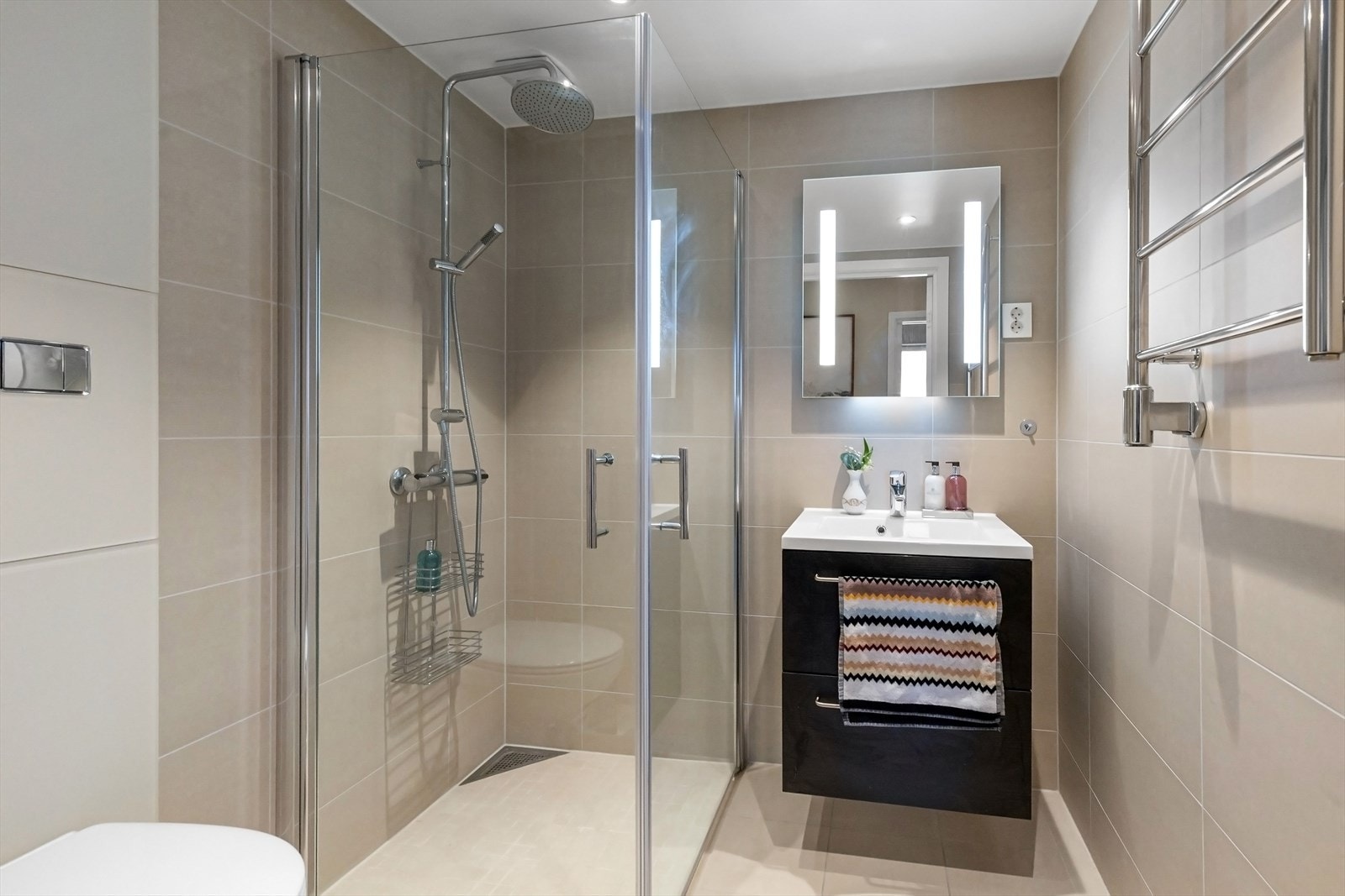 Bad 2 med dusj med innfellbare dører i herdet glass, servant og veggfestet klosett med innebygget sisterne. Overflatene er flislagt i lyse og delikate farger. Varmekabler i gulv. Galleribilde