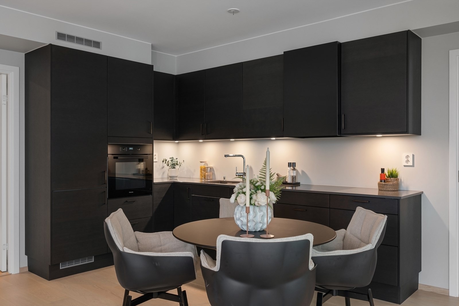 Velutstyrt Sigdal kjøkken med mørke glatte skapfronter. Benkeplate med vaskekum og Miele induksjon platetopp. Galleribilde