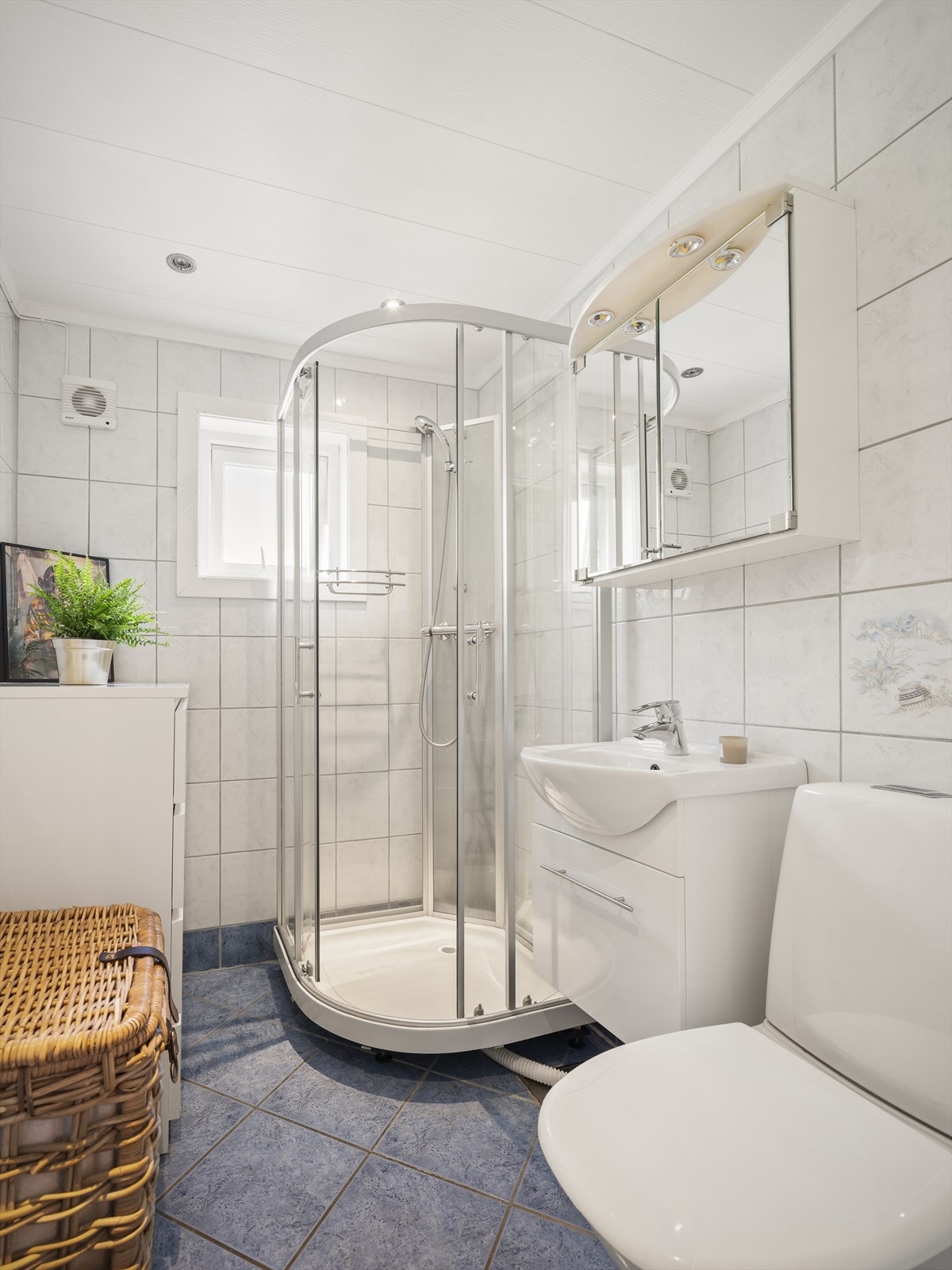 Lys baderomsinnredning med vask fra 2015, speilskap med belysning over. Baderommet er også utstyrt med dusjkabinett fra 2015, samt gulvstående toalett fra 2015. Galleribilde