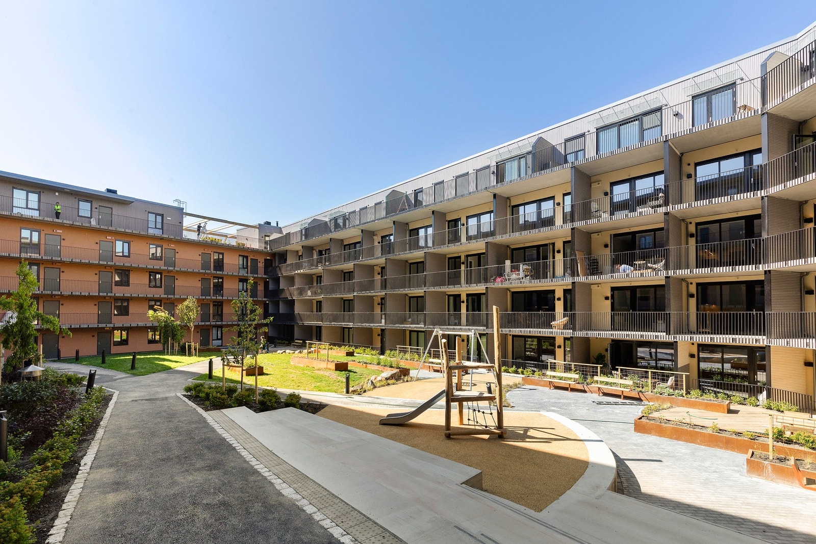 Stor, grønn opparbeidet felleshage i bakgården med blant annet gressplen, sitteplasser og lekestativ Galleribilde