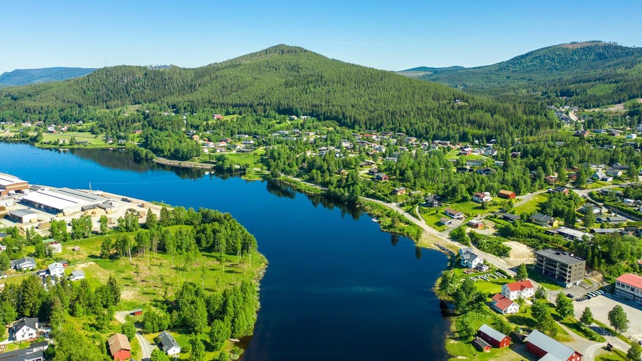 Tomten ses oppe til høyre i bildet. I front Trysilelva og bak ligger Grimsåsen, et populært friluftsområde med stier for sykkel, til fots og på ski. Foto Jonas Sjøgren Galleribilde
