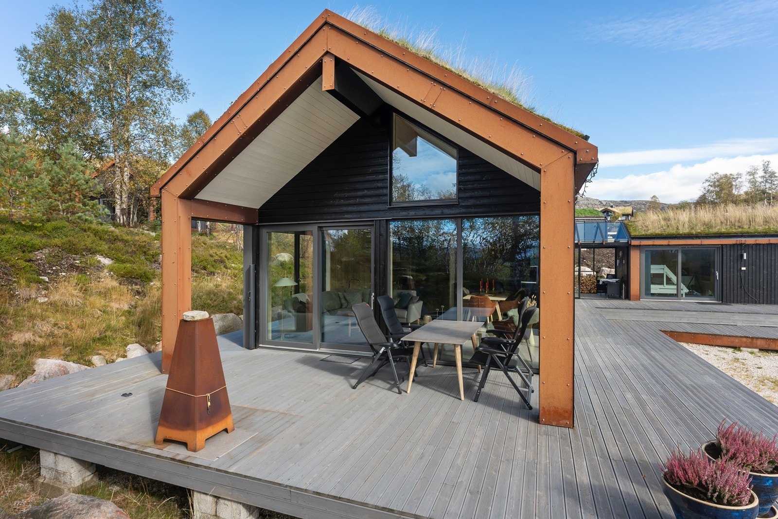 Både hoveddelen og annekset er utformet i samme stil med torvtak, mørkbeisede vegger i panel og detaljer i stilig cortenstål med rustrød overflate Galleribilde