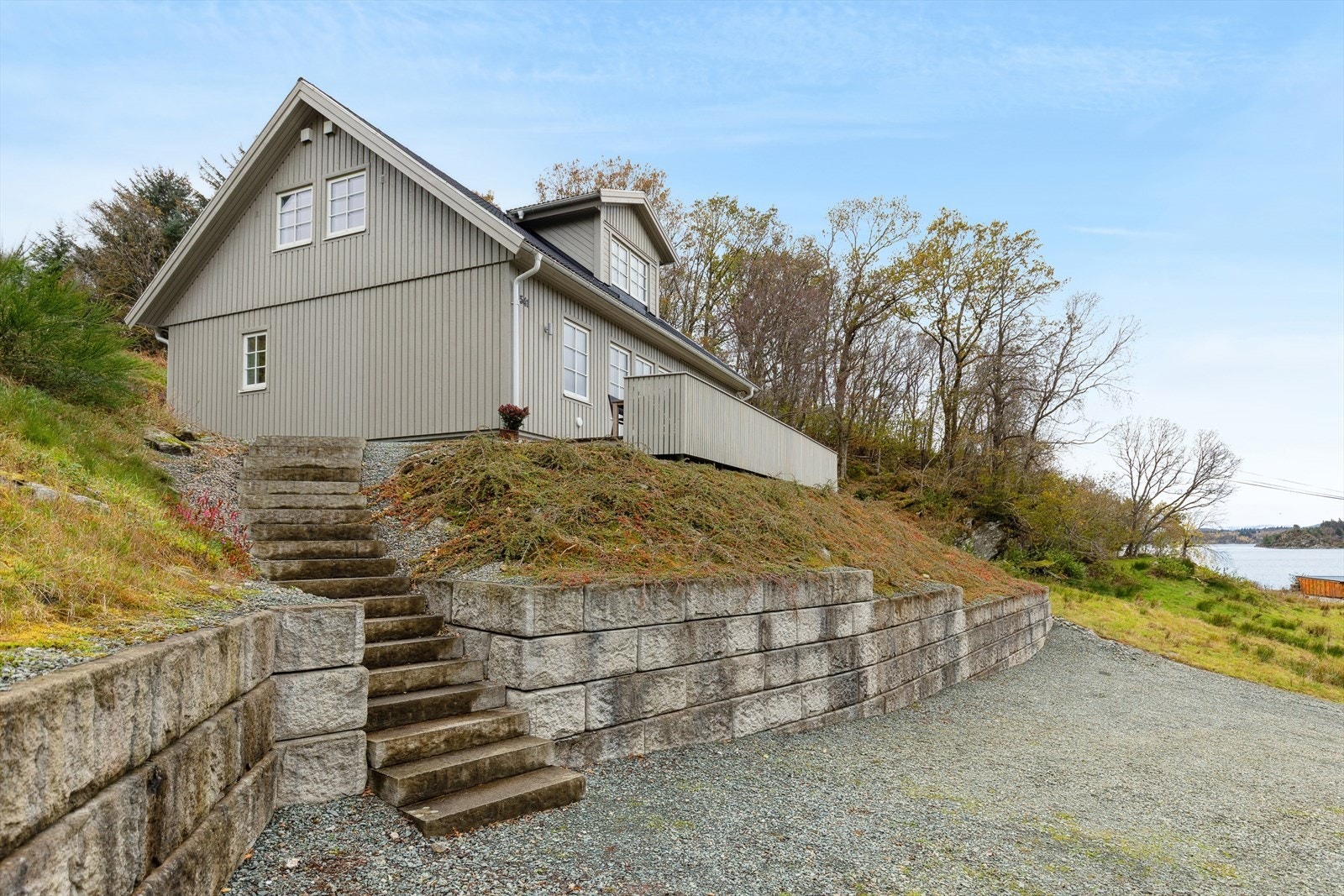 Eiendommen har god plass til parkering på gruset gårdsplass. Støttemuren i solide steinblokker gir et ryddig og stabilt preg. Galleribilde