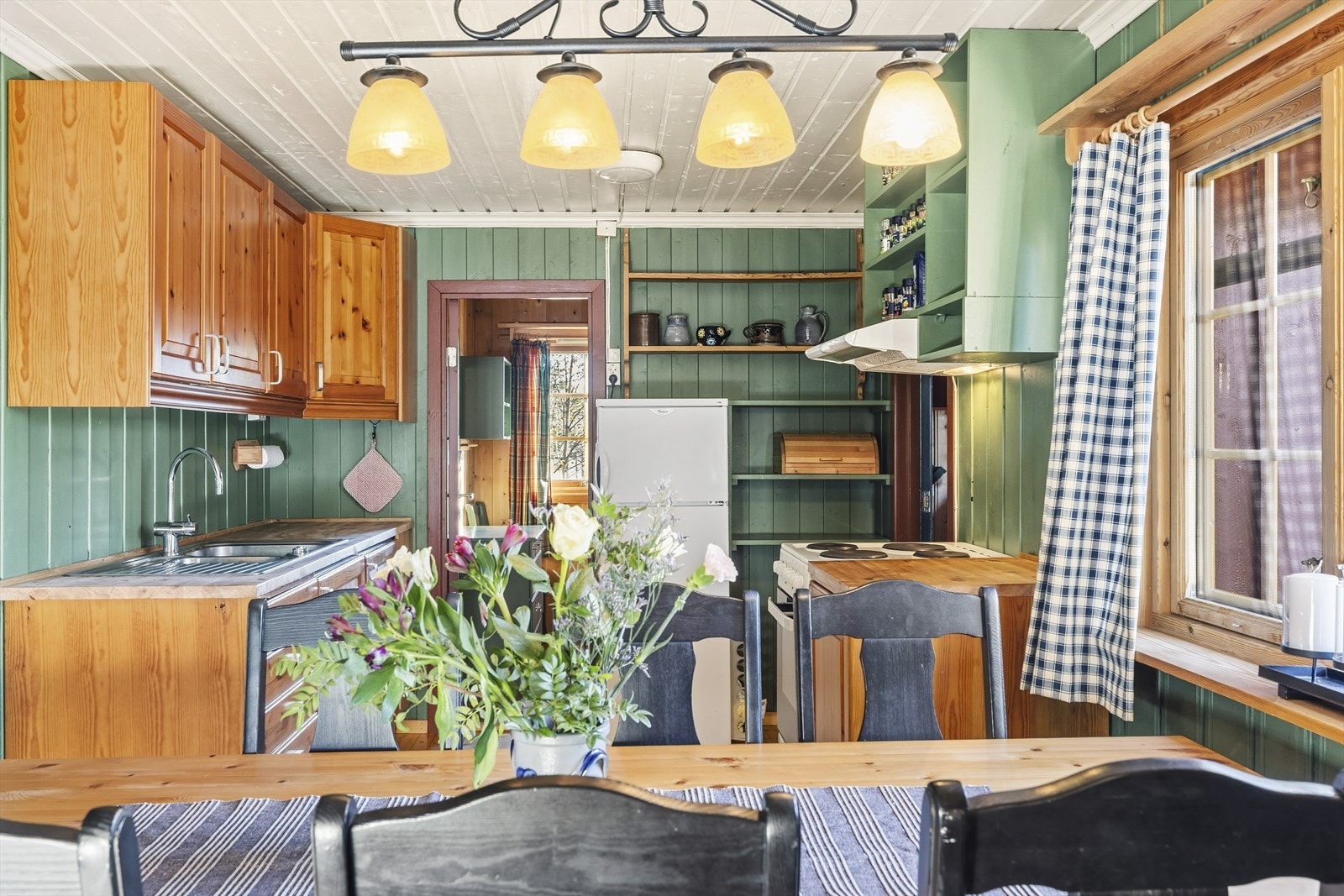 Innredning inneholder vask, frittstående kjøleskap, og komfyr med mekanisk vifte. Galleribilde