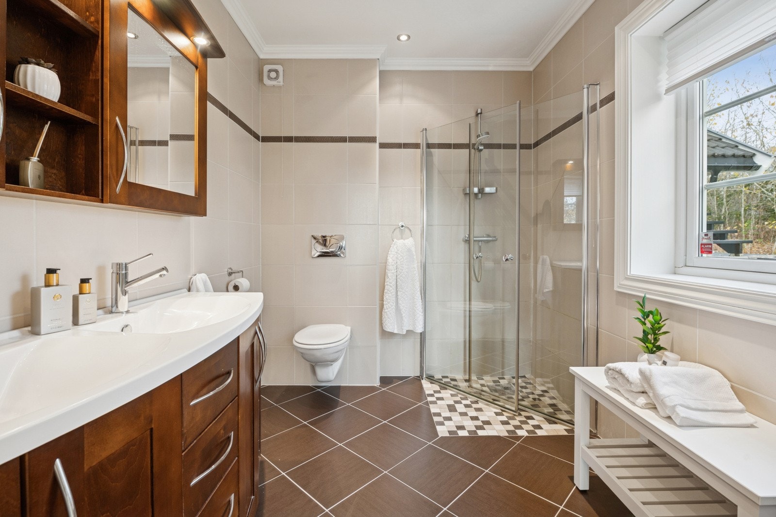 Badet har flislagte overflater, dusjhjørne med glassvegger, dobbel servant, god oppbevaringsplass og varmekabler i gulv for ekstra komfort. Galleribilde