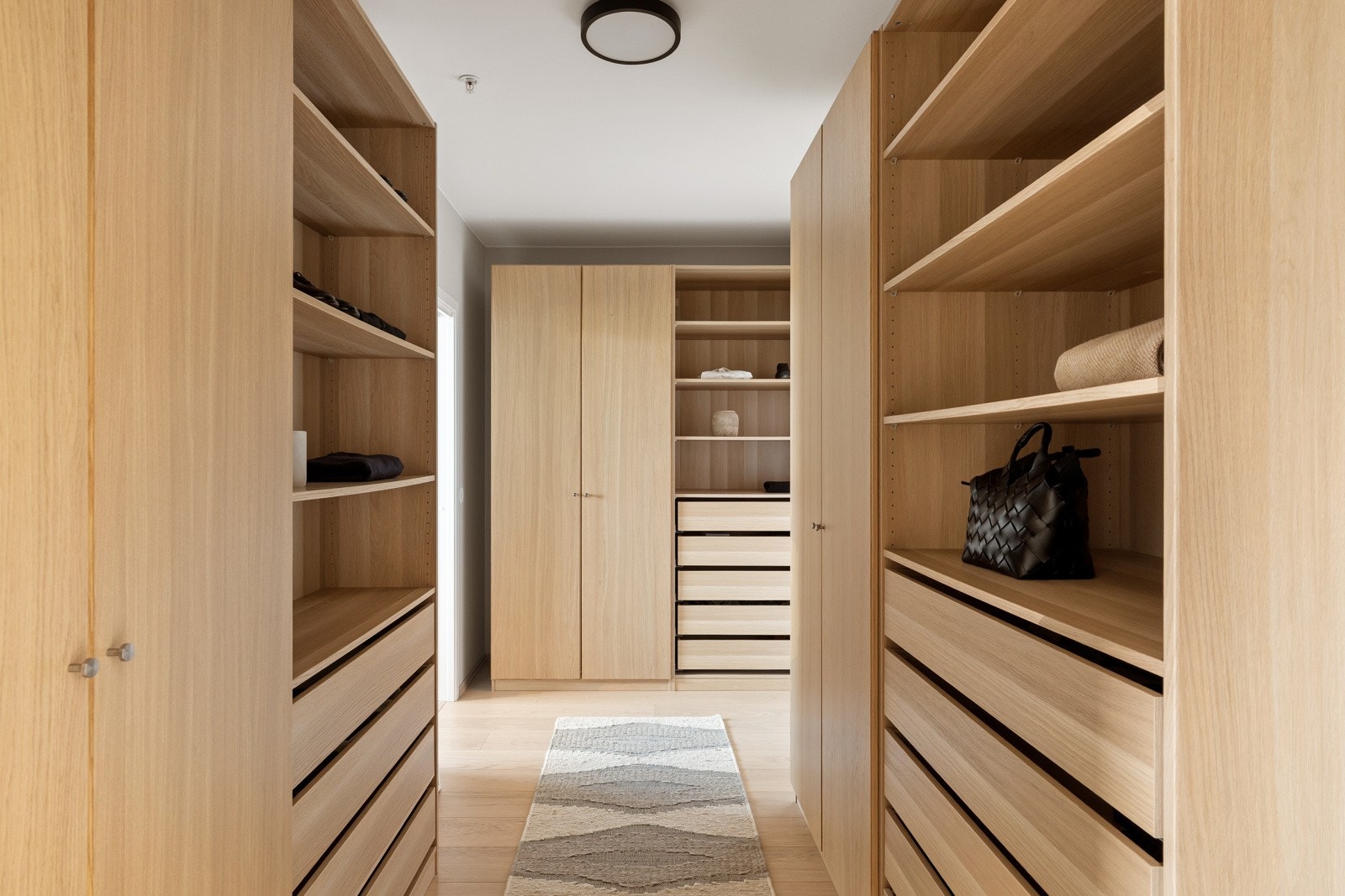 Omkledningsrommet er innredet med flere garderobeskap og åpne skap i eikefinish med rikelig innredning, hyller og skuffer Galleribilde