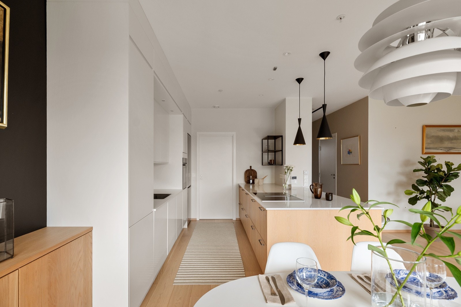 Både halvøya og vaskebenken langs veggen har benkeplate i lys, tynn stein og ved benken er det backsplash i samme materiale. Galleribilde