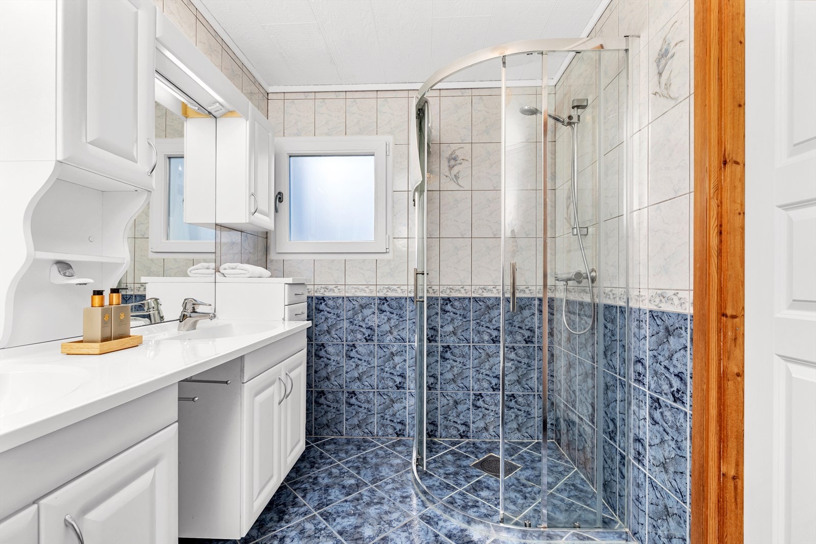 Badet er innredet med dusjhjørne og baderomsmøbler i hvit utførelse Galleribilde