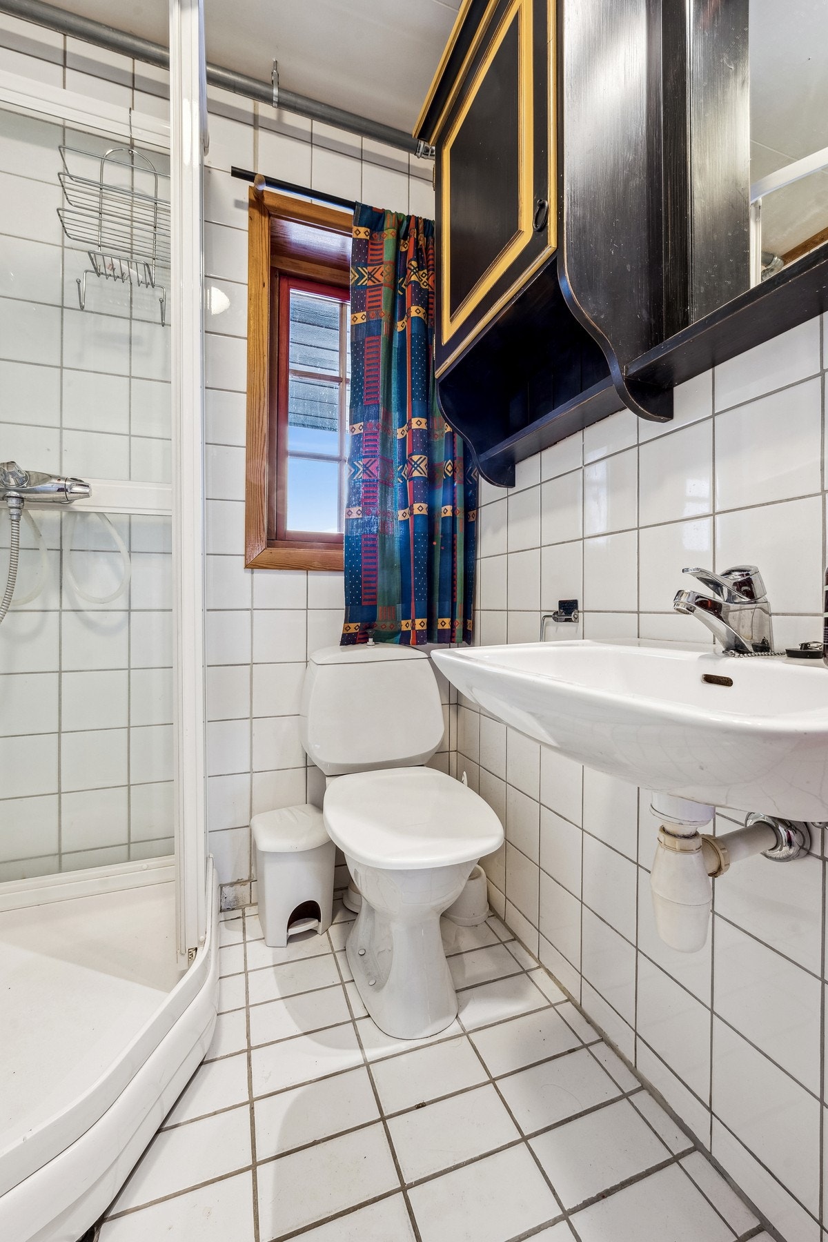 Badet består av vegghenget servant med armatur, dusjkabinett med dusjarmatur, tørkeskap og gulvstående toalett. Galleribilde