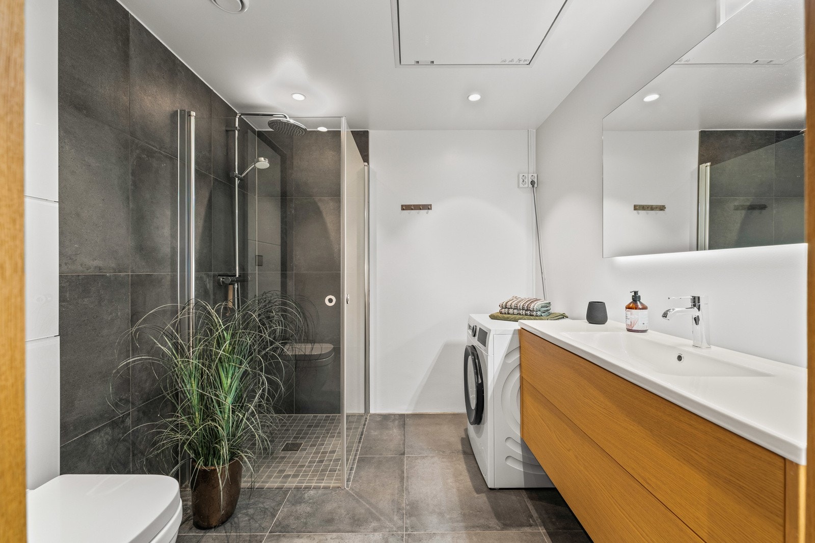 Delikat, flislagt bad med dusjhjørne, opplegg for vaskemaskin og servant med underskuffer Galleribilde