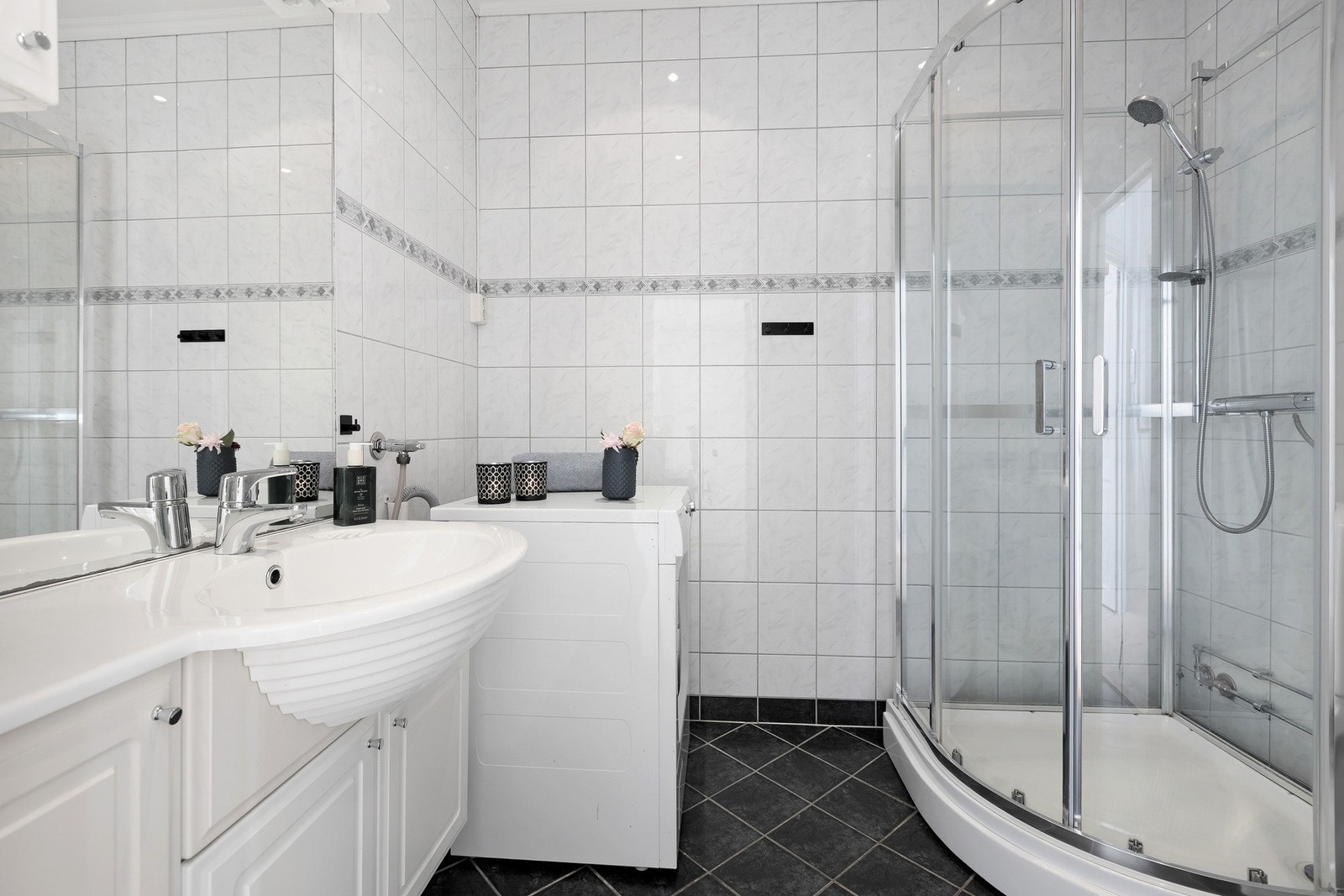 Pent bad med lyse fliser, servantinnredning med god lagringsplass og dusjkabinett. Galleribilde