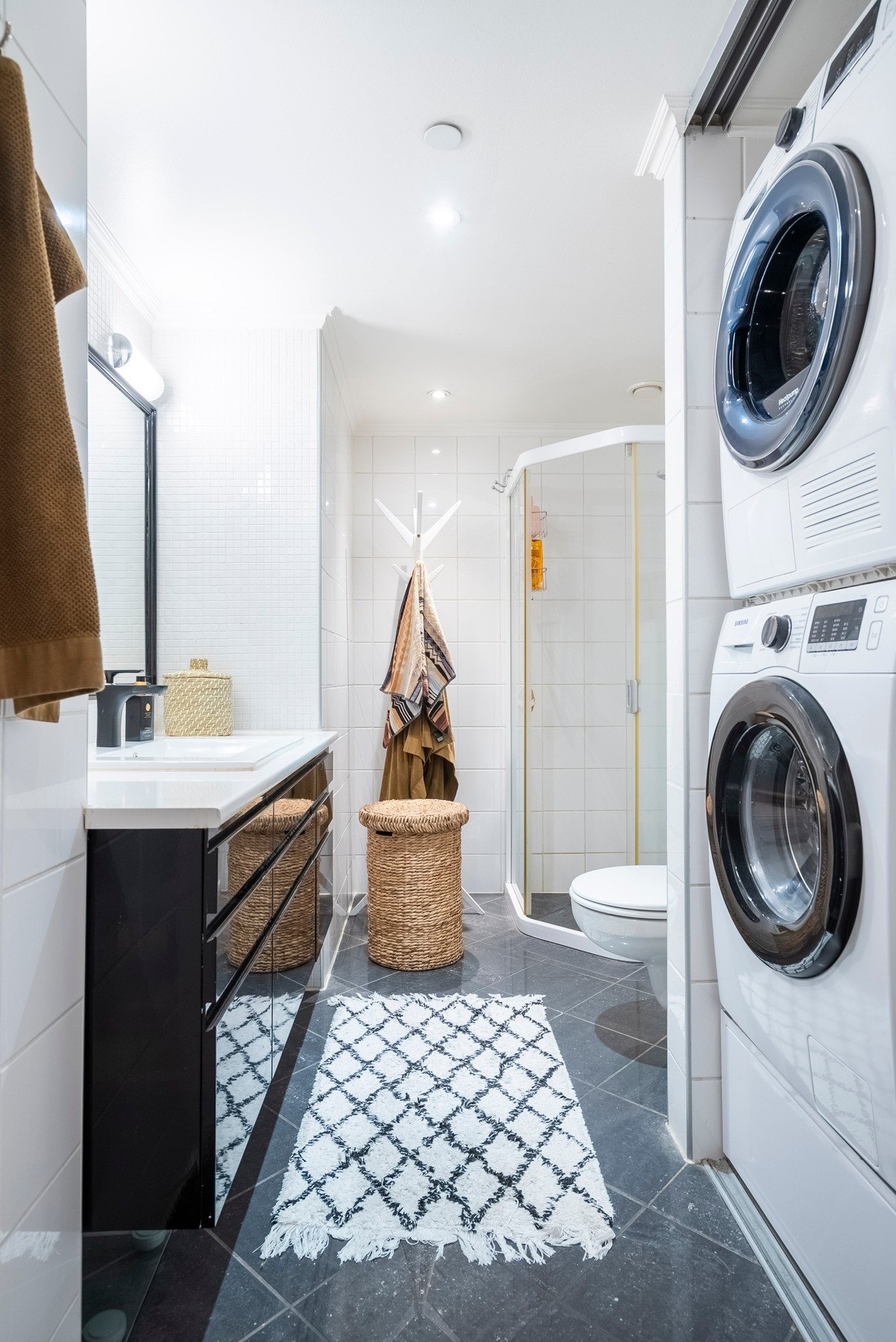 Tidløst flislagt bad med varmekabler i gulvet og eget område bak skyvedører til vaskemaskin og tørketrommel Galleribilde
