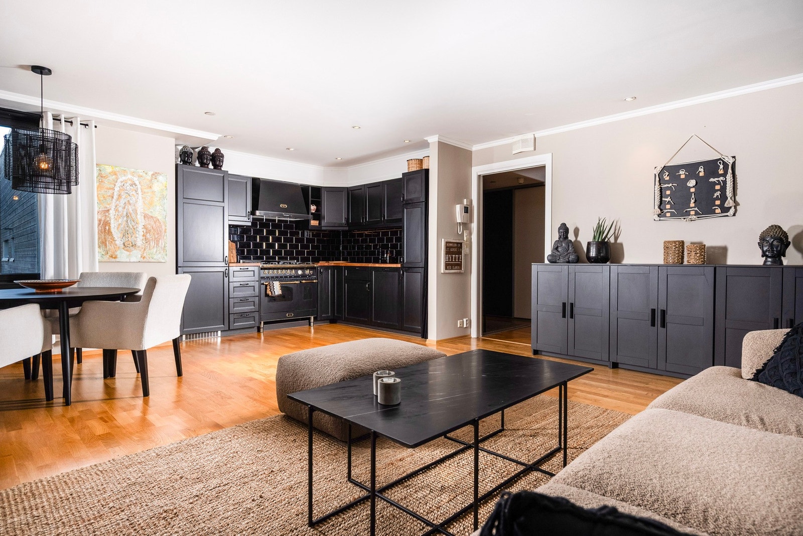 Stue og kjøkken i åpen løsning, hvor den mørke kjøkkeninnredningen og flisene definerer kjøkkenområdet Galleribilde