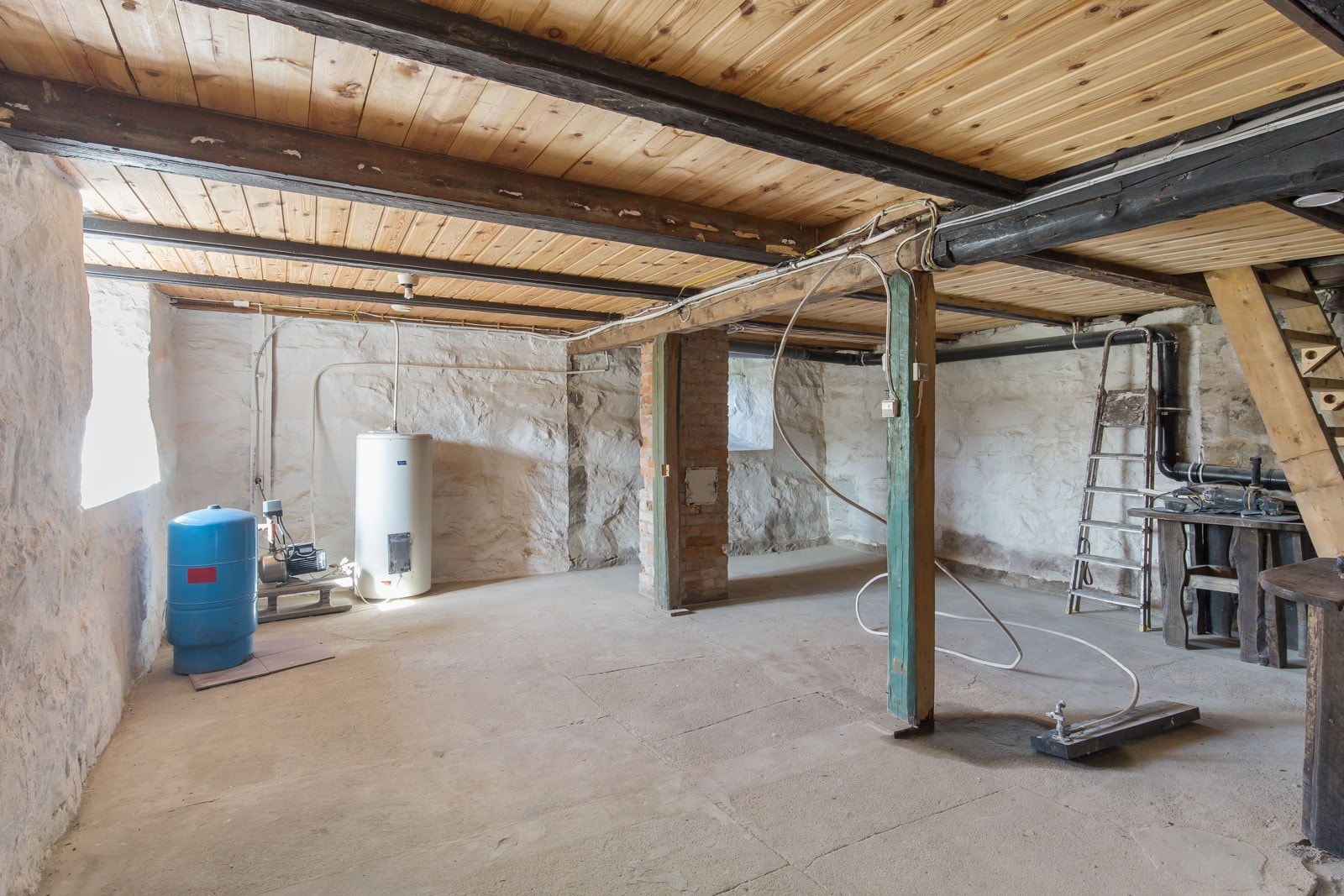 Romslig kjeller med synlige bjelker, varmtvannsbereder og tekniske installasjoner. Galleribilde