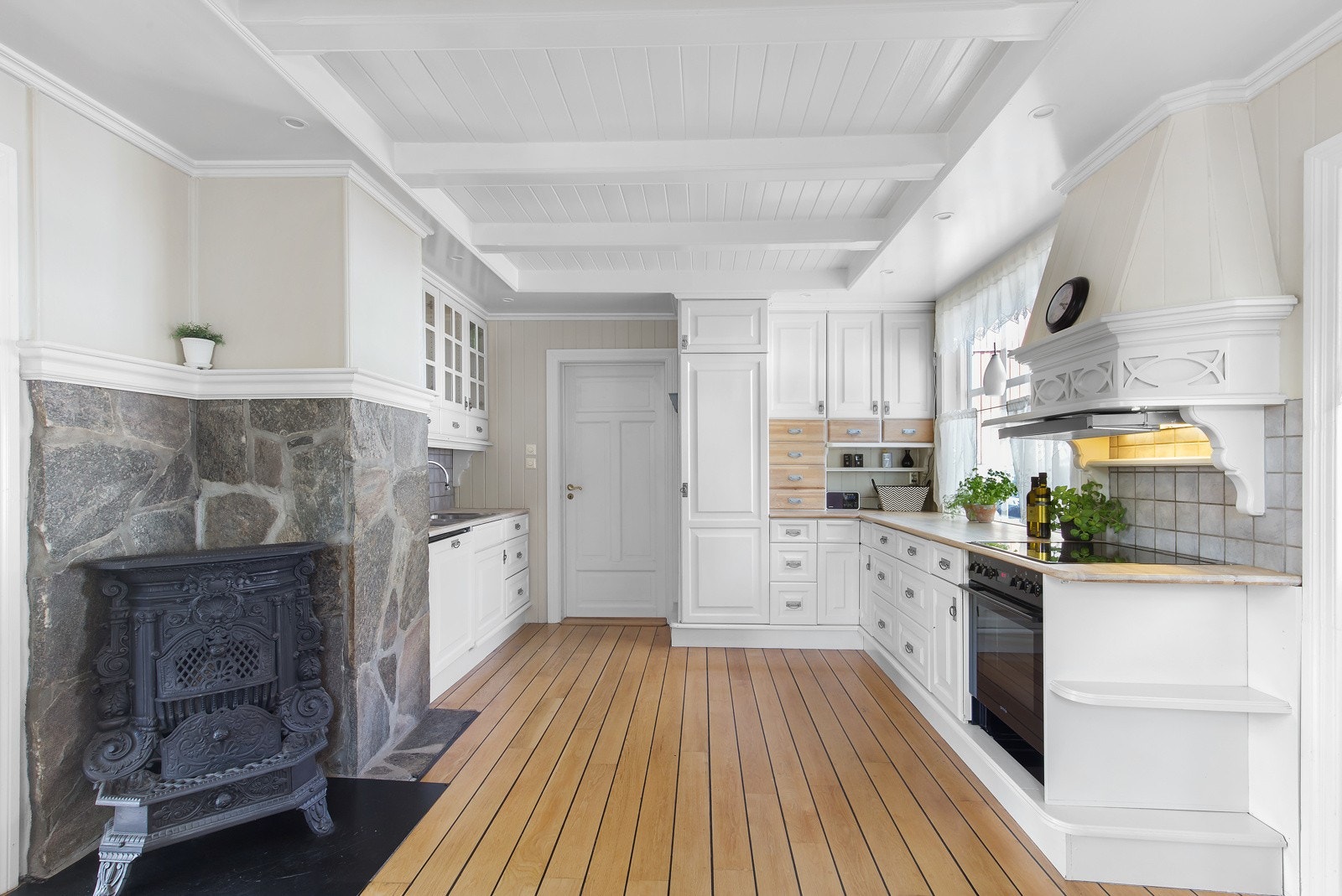 Kjøkkenet har hvite skap, peis med steinmur og integrerte hvitevarer. Galleribilde