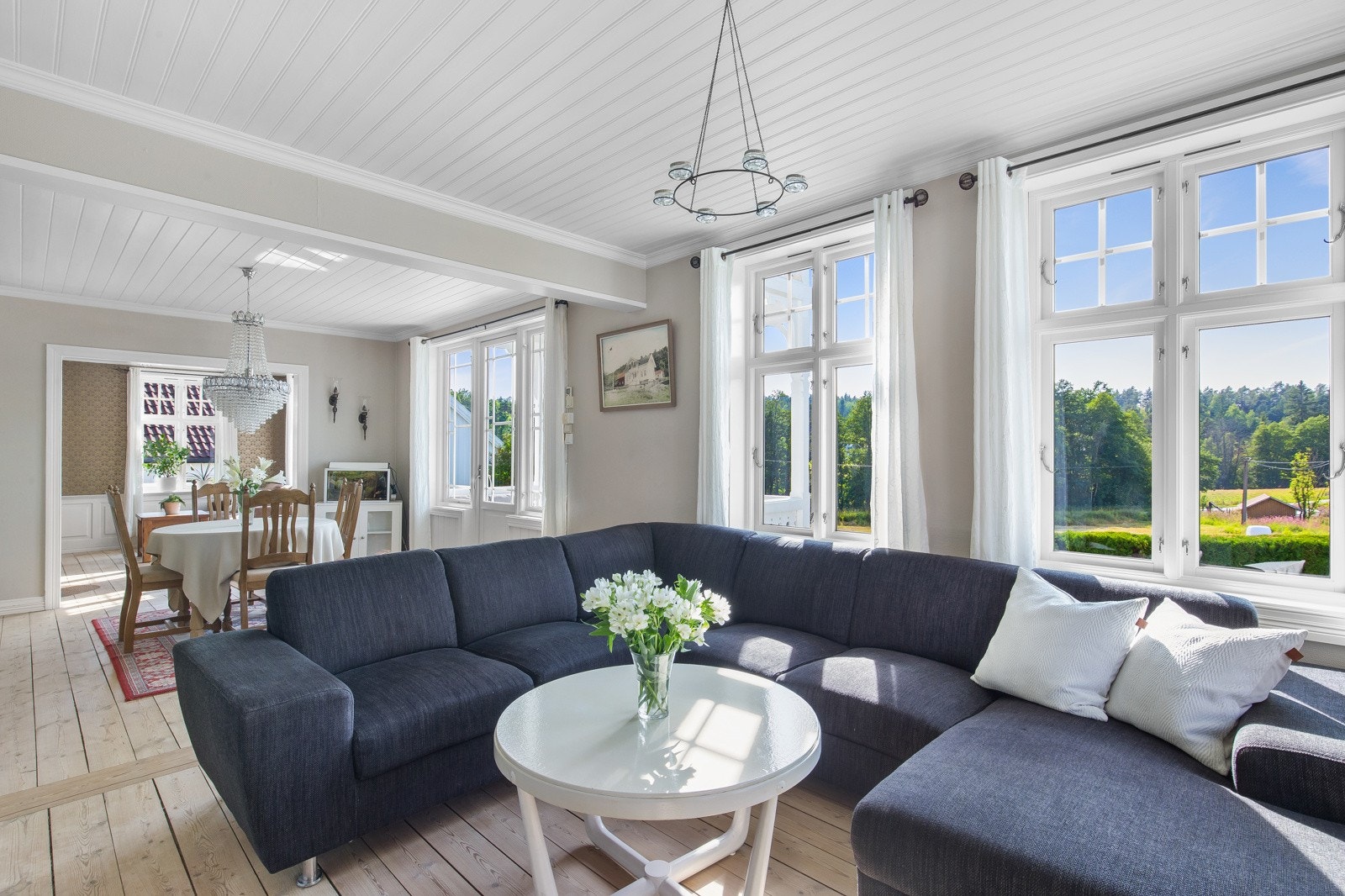 Lyst stueområde med store vinduer, åpen løsning til spisestue og grønt utsyn. Galleribilde