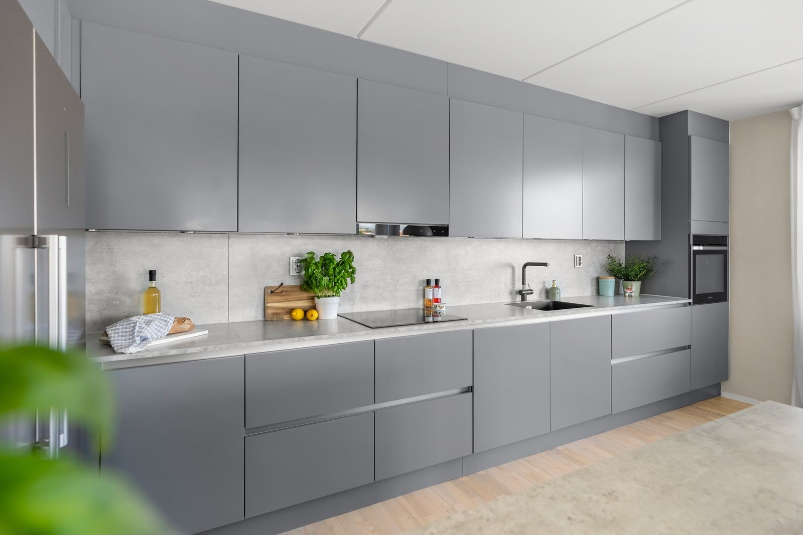 Stilrent HTH-kjøkken med glatte fronter og laminat benkeplate med underlimt vask, belysning og plate over benken. Galleribilde