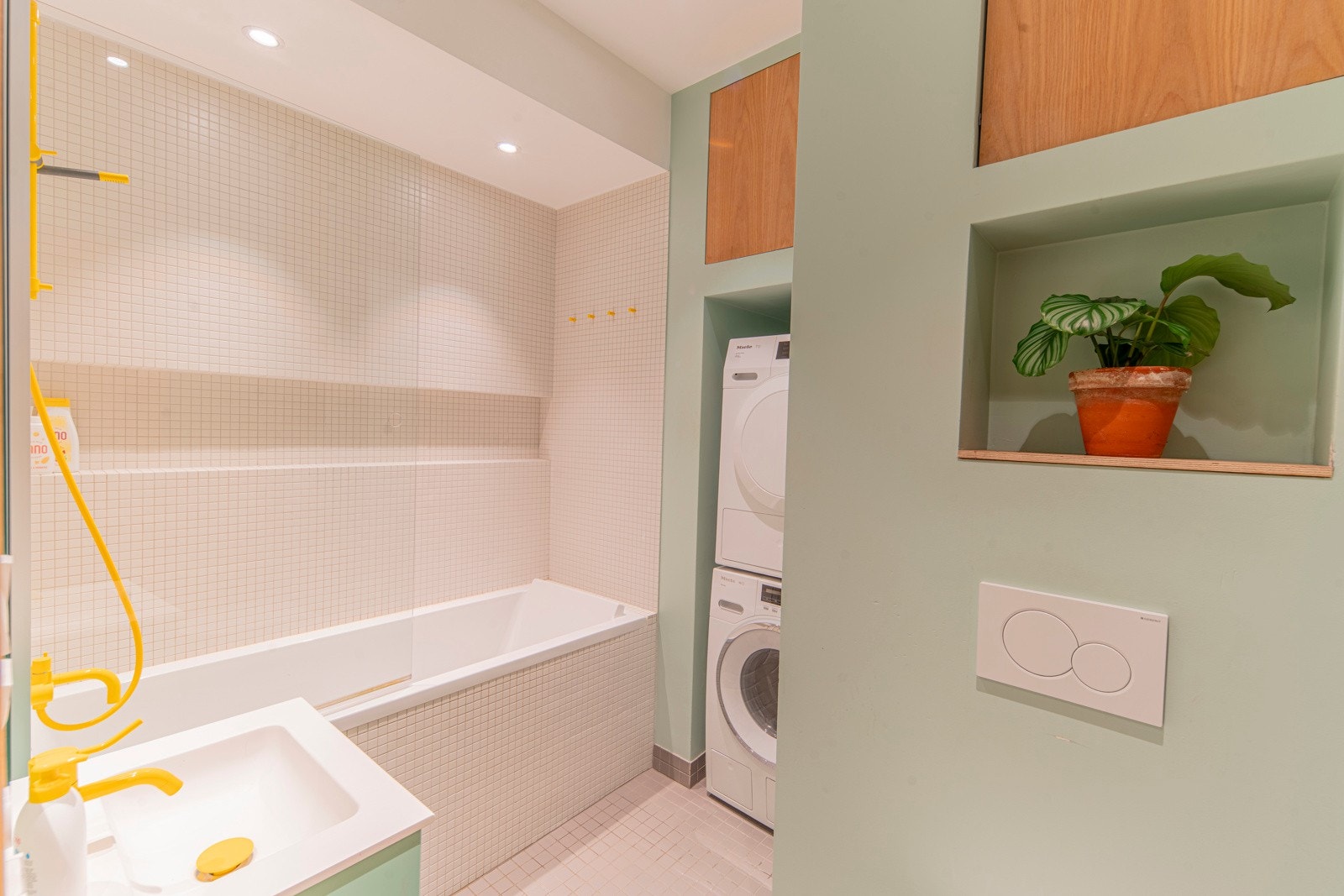 Praktisk bad/vaskerom med hvite mosaikkfliser, badekar/dusj + wc. Vaskesøyle med vaskemaskin og tørketrommel i nisje. Varmekabler i gulv. Elektrisk vifte. Galleribilde